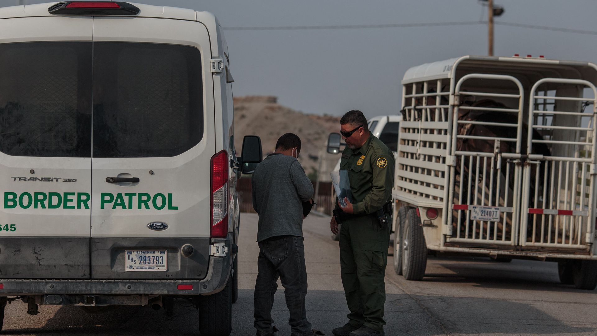 Photo of a Border Patrol officer with a migrant next to a parked van that says "Border Patrol"