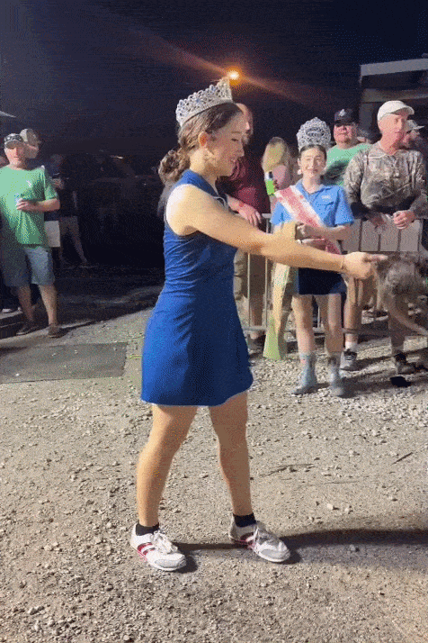 Image shows a woman in a crown throwing a dead nutria.
