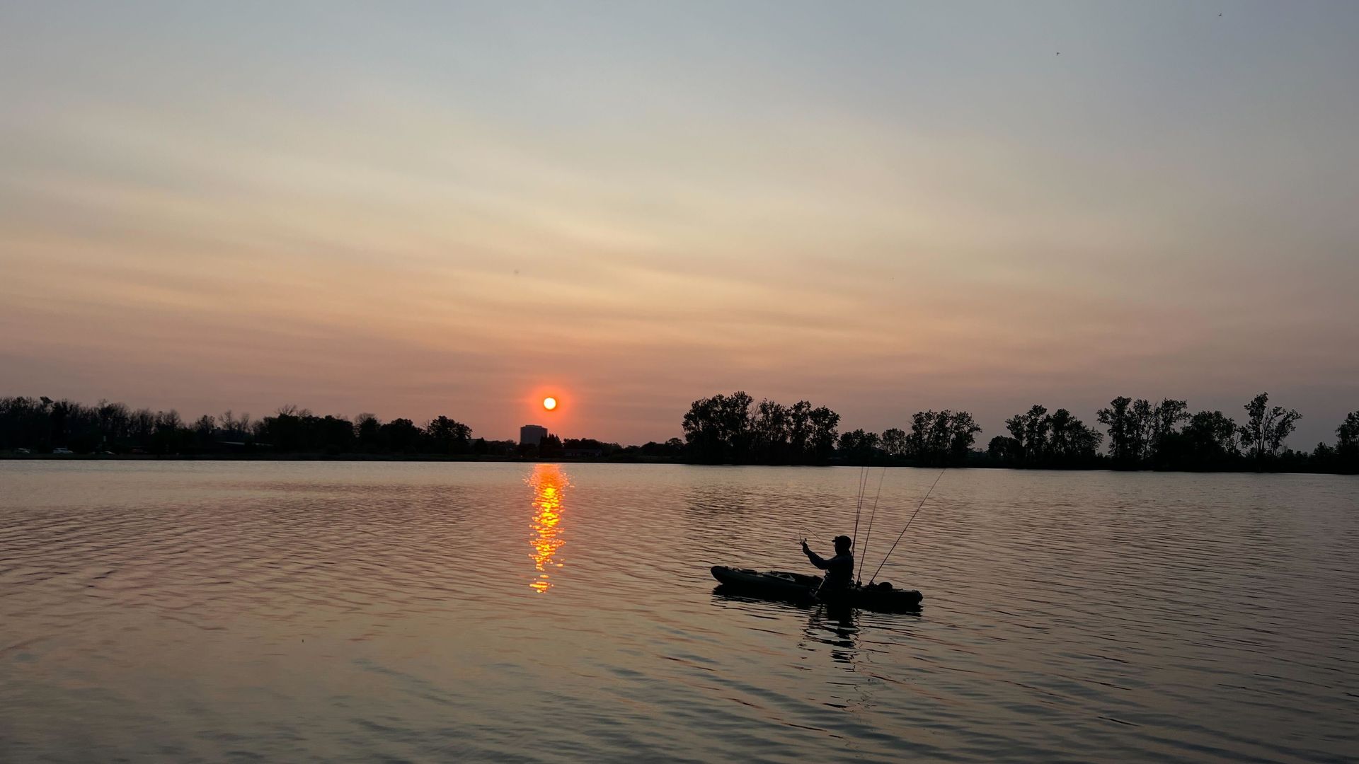 The sun sets on the Detroit River with a kayaker in views.