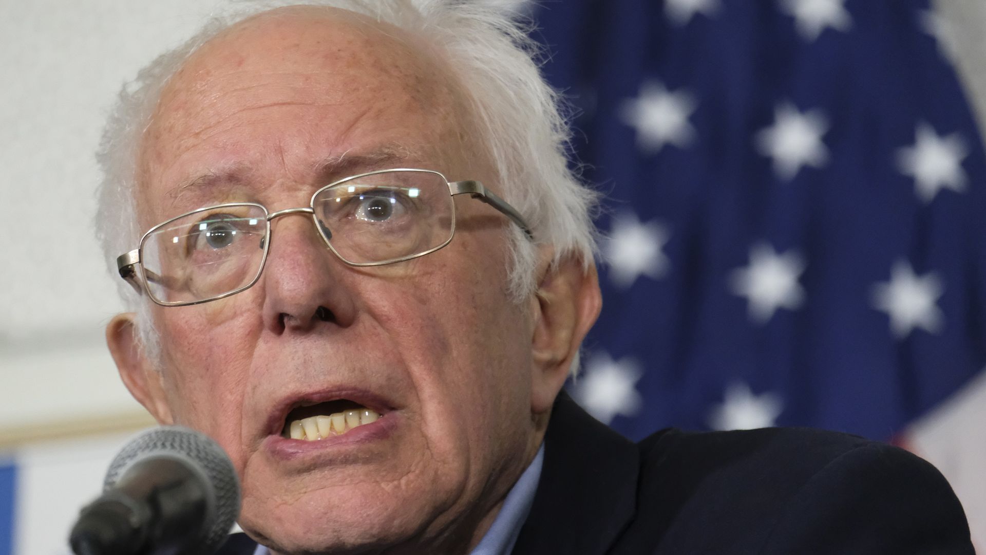In this image, Bernie Sanders speaks into a microphone. 