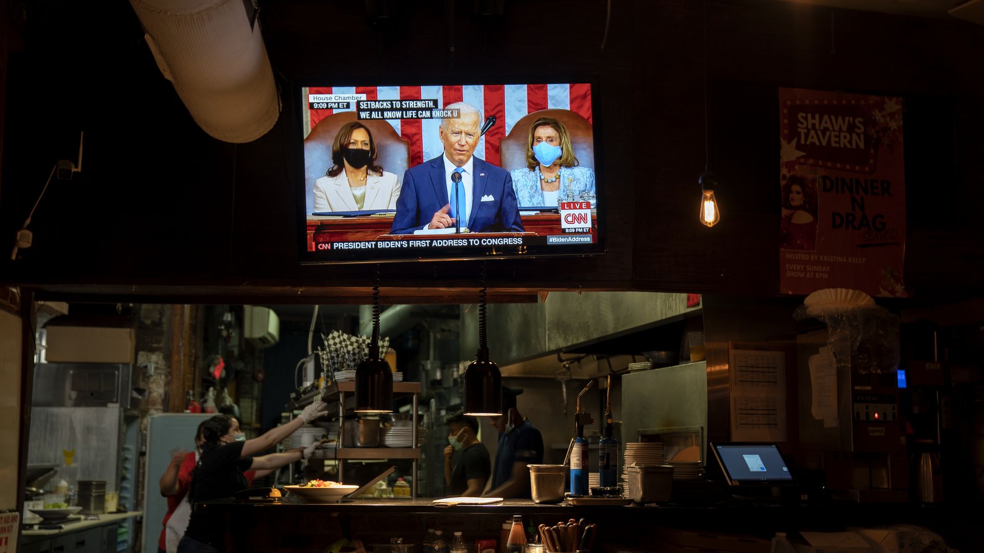 Photo of a TV screen showing Biden as he gives a speech, the TV hangs over a kitchen space in a restaurant