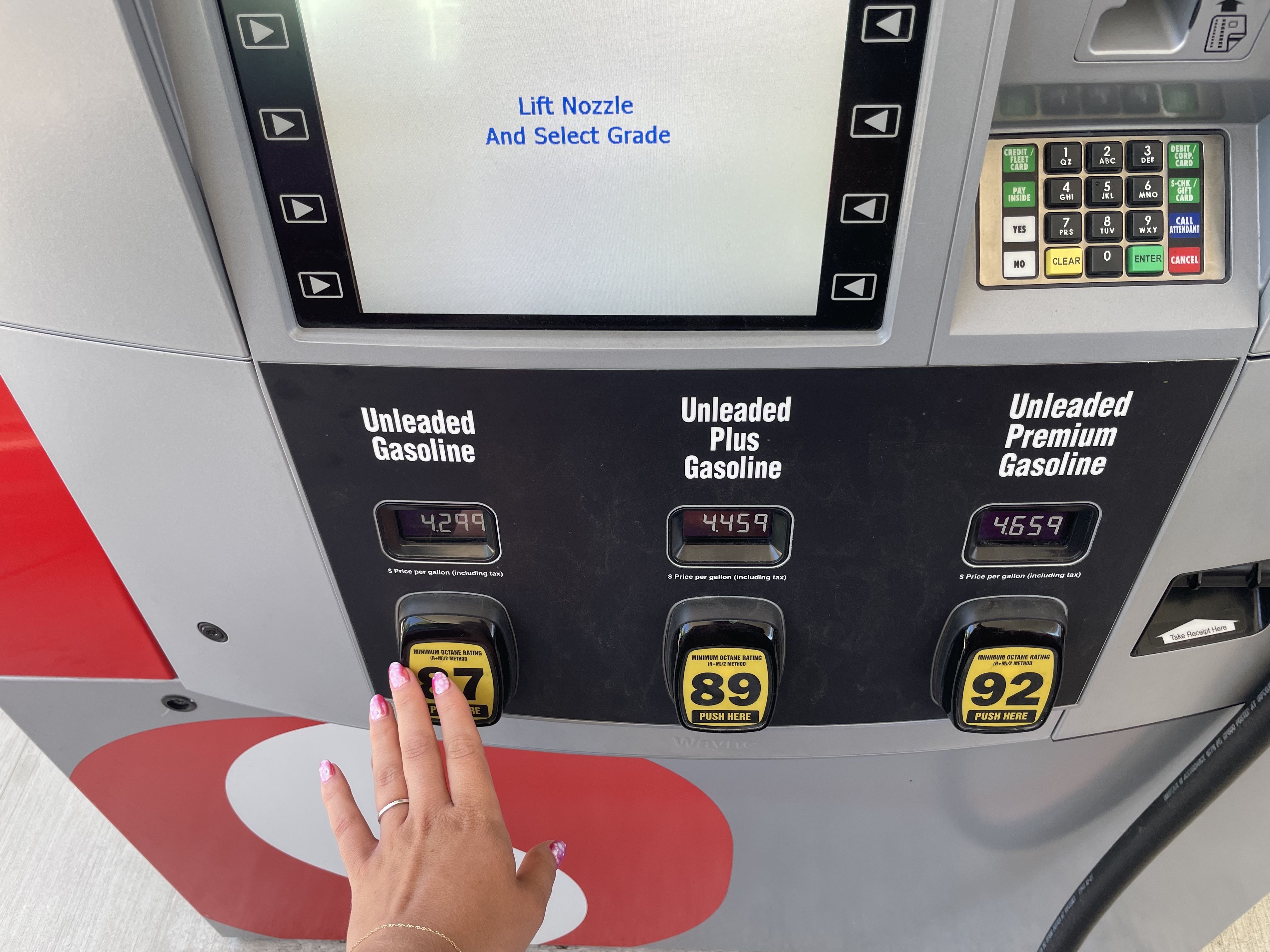 An image of a hand selecting a gasoline grade at a gas pump.