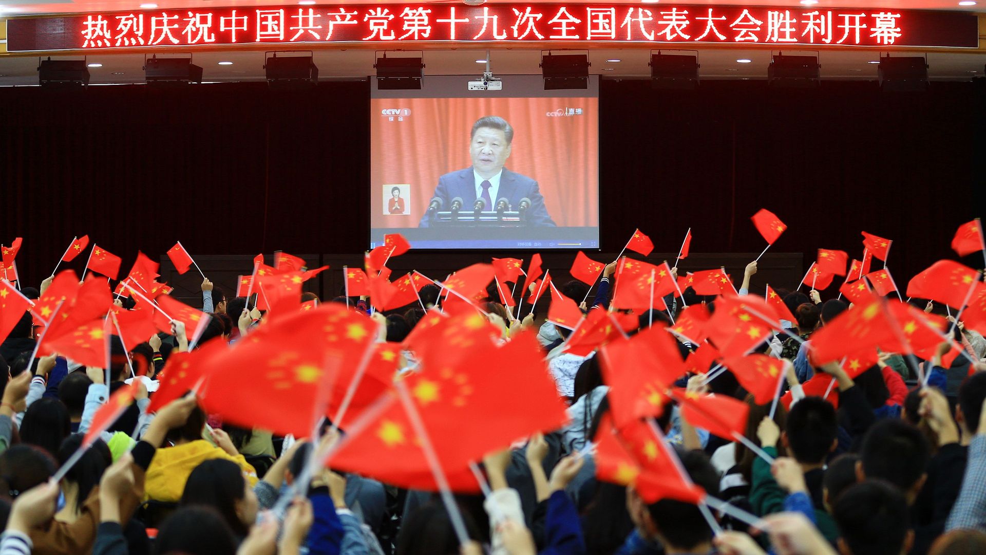 College students waiving Chinese flags in school stadium watching Xi Jinping speak on screen