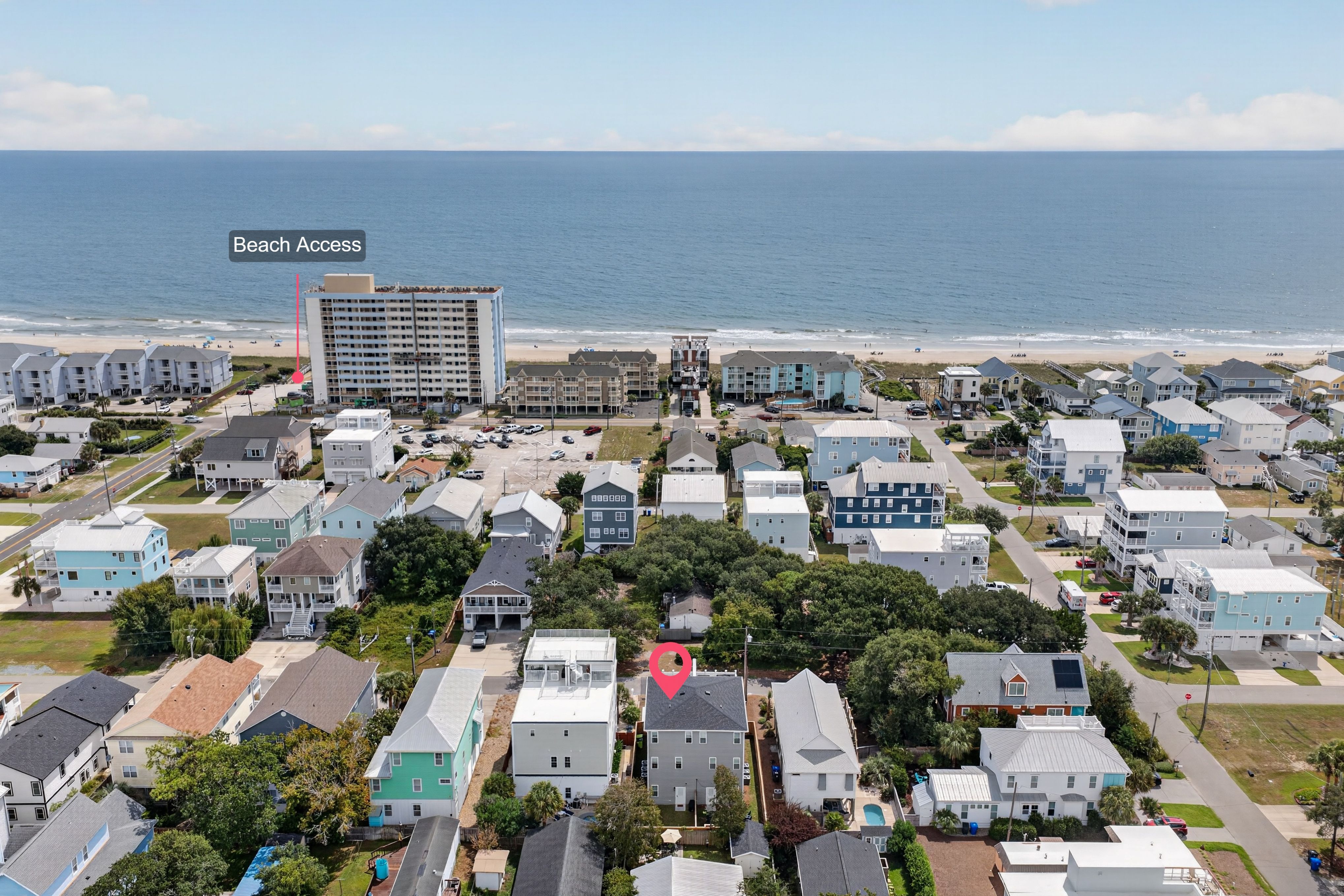 An aerial view of a coastal town: a tall beachside hotel, colorful houses, and a blue ocean. A "Beach Access" label with a pink pin marks the path near the hotel.