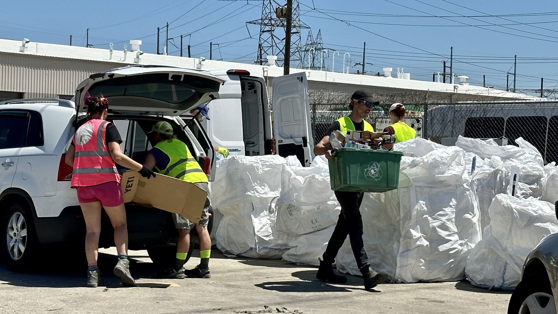 Photo shows people emptying recycling out of the trunk if a vehicle.