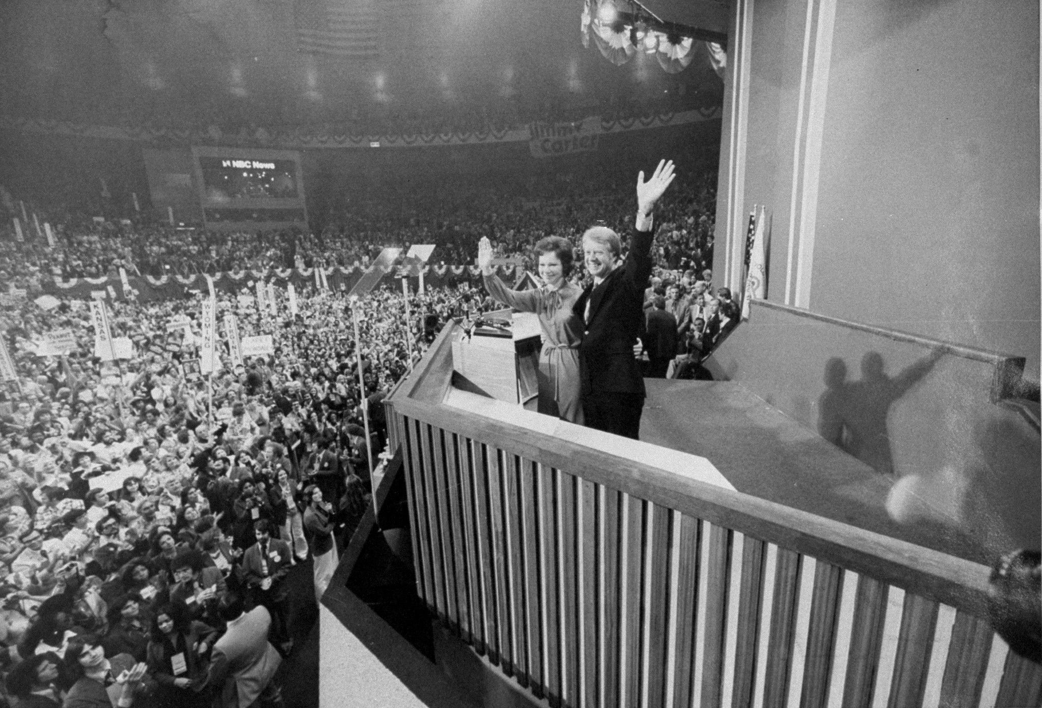 Black and white photo of Jimmy Carter waving to a huge crowd at the 1976 Democratic National Convention after he accepted the nomination. Next to him is wife, Rosalynn, also waving