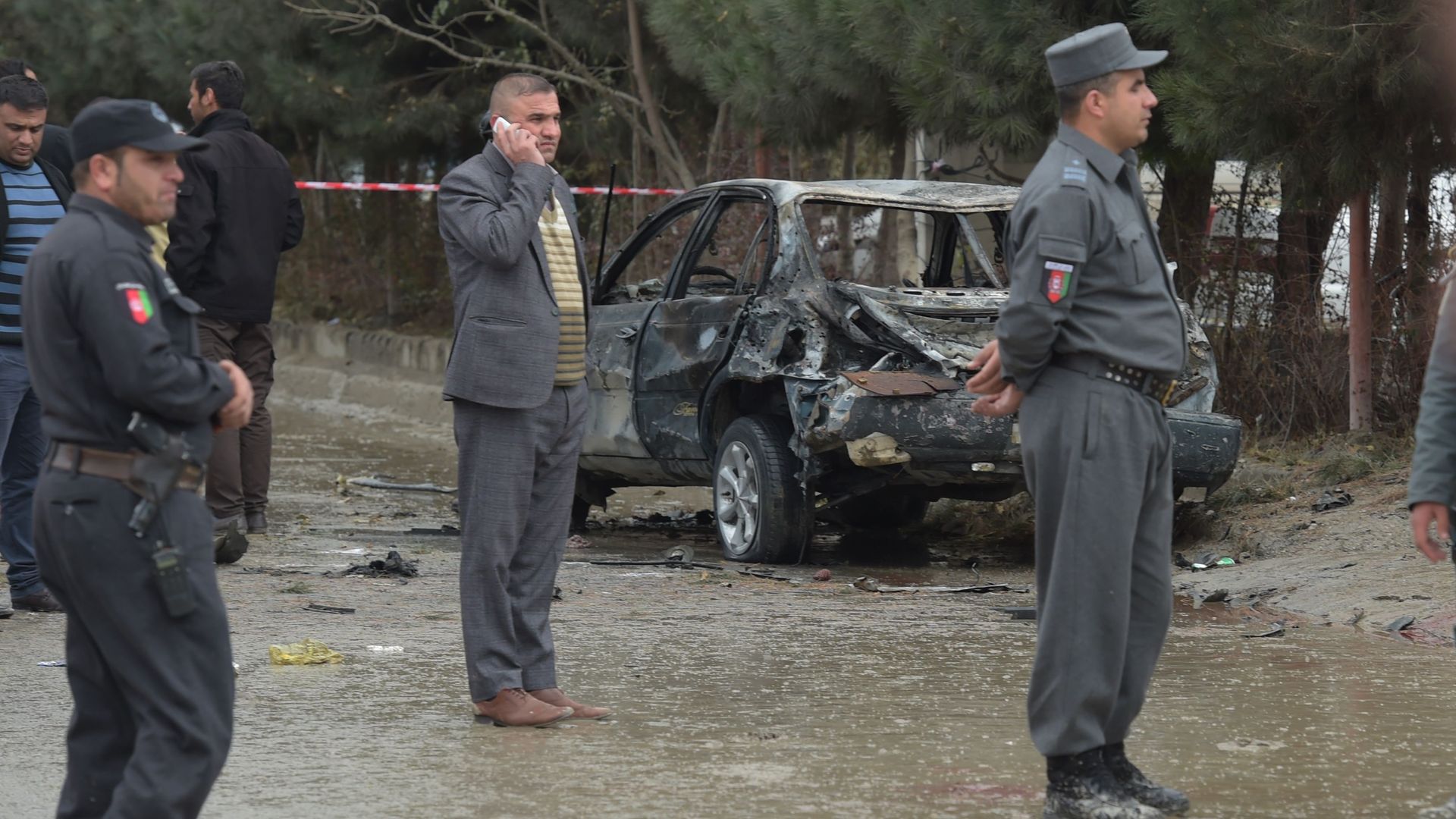 Afghan security personnel standing next to burnt-out car