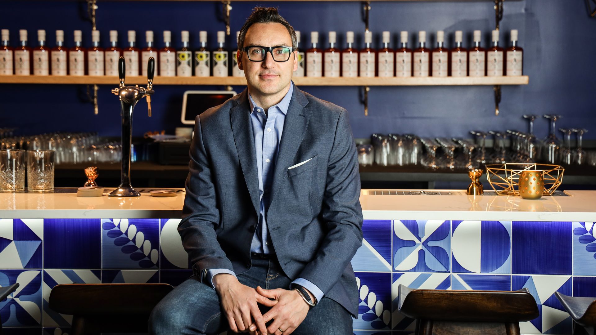 Francesco Amodeo behind a wall of bottles and Italian ceramic tile at his distillery in DC's Ivy City neighborhood, Don Ciccio & Figli