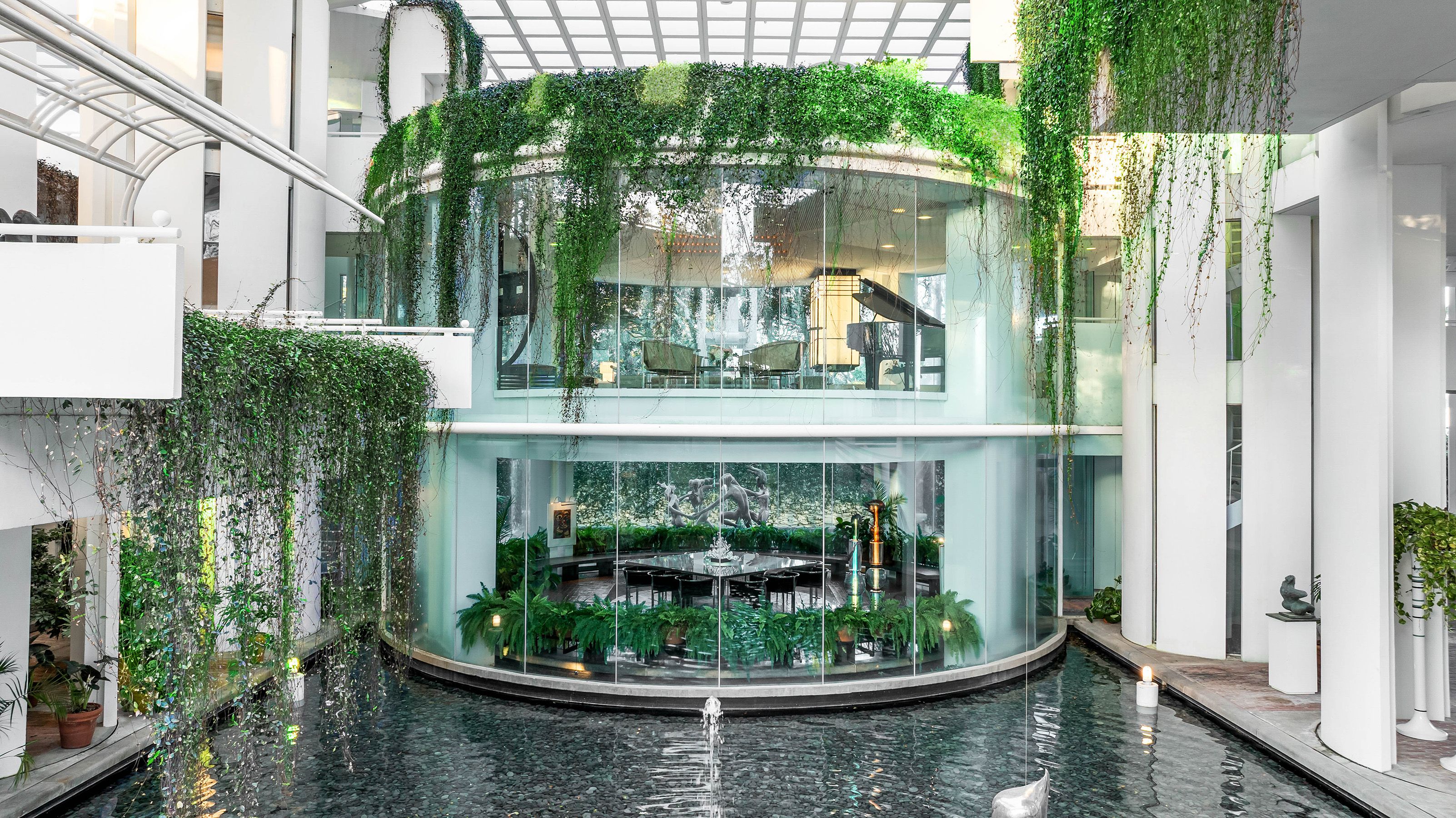 A photo of a multi-story atrium with ivy covered windows overlooking a shallow pool 