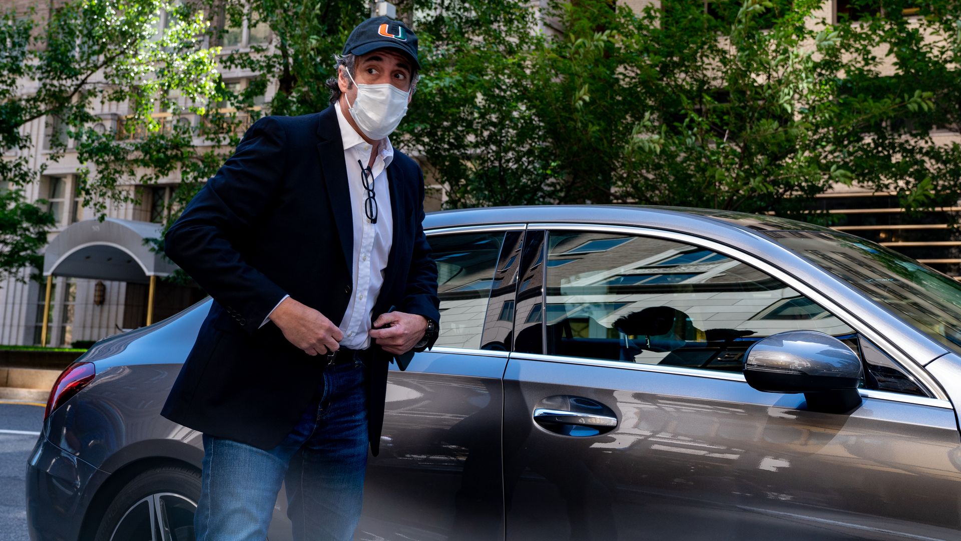 Michael Cohen stands wearing a mask outside of a car