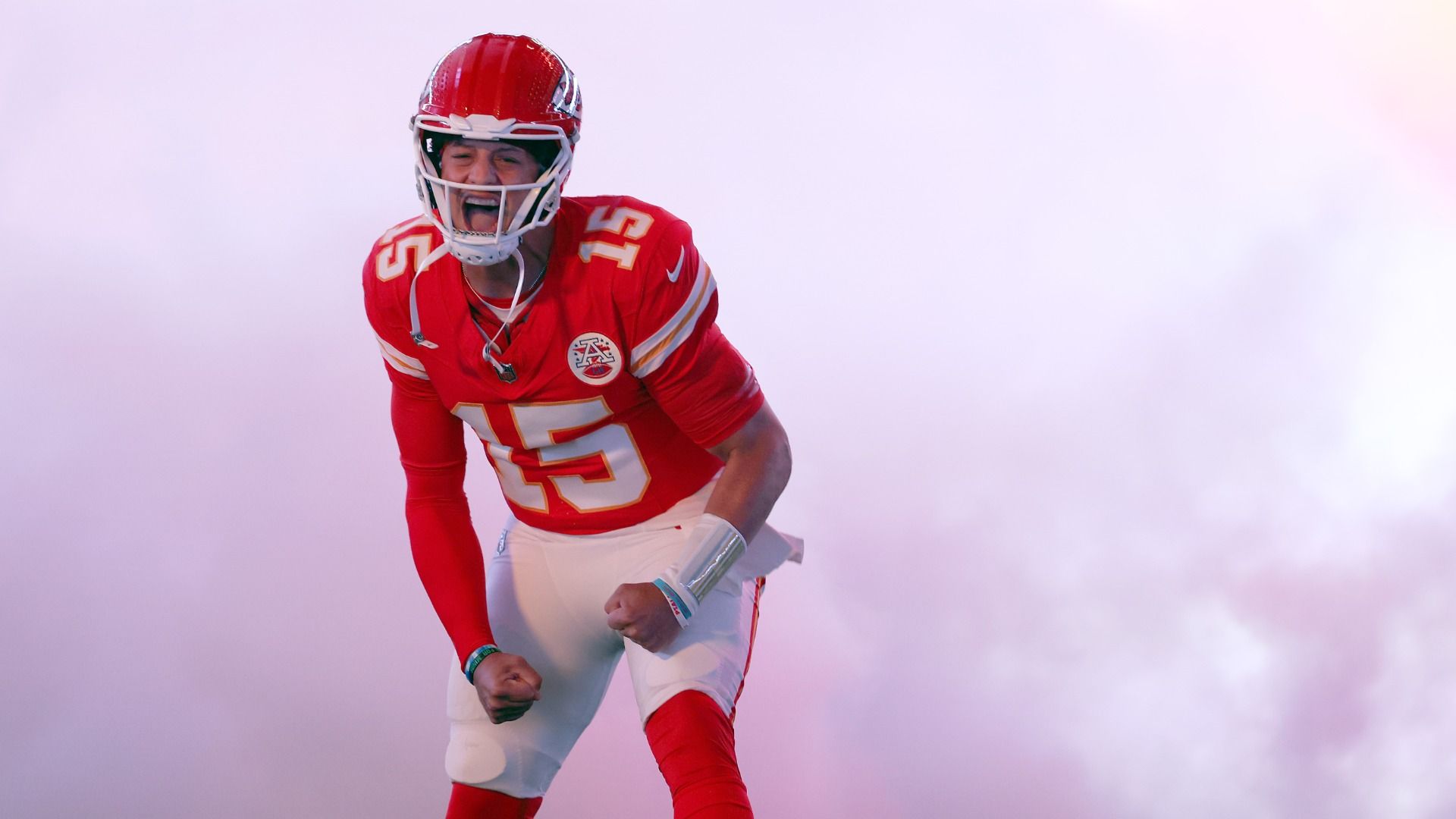 Chiefs quarterback Patrick Mahomes flexes and yells in front of a foggy background before the start of a football game.