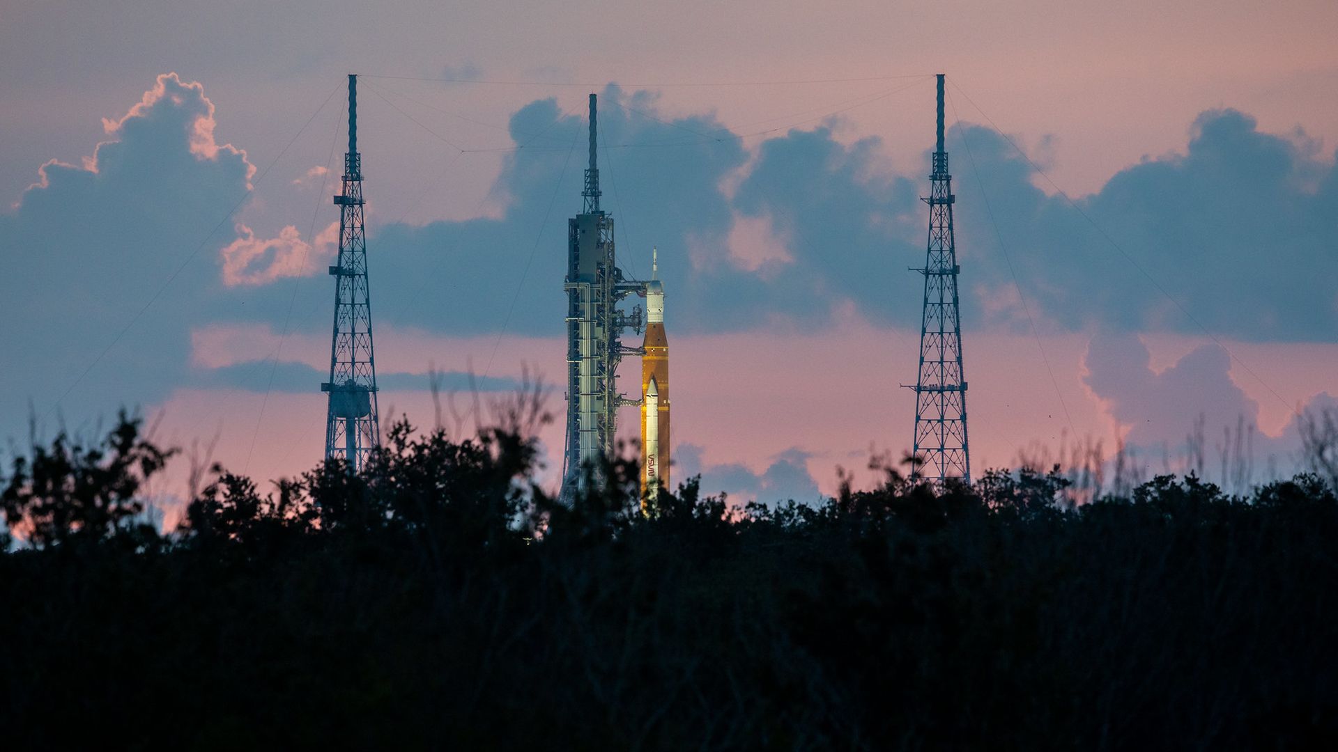 The space launch system rocket standing on the pad against a pink sky