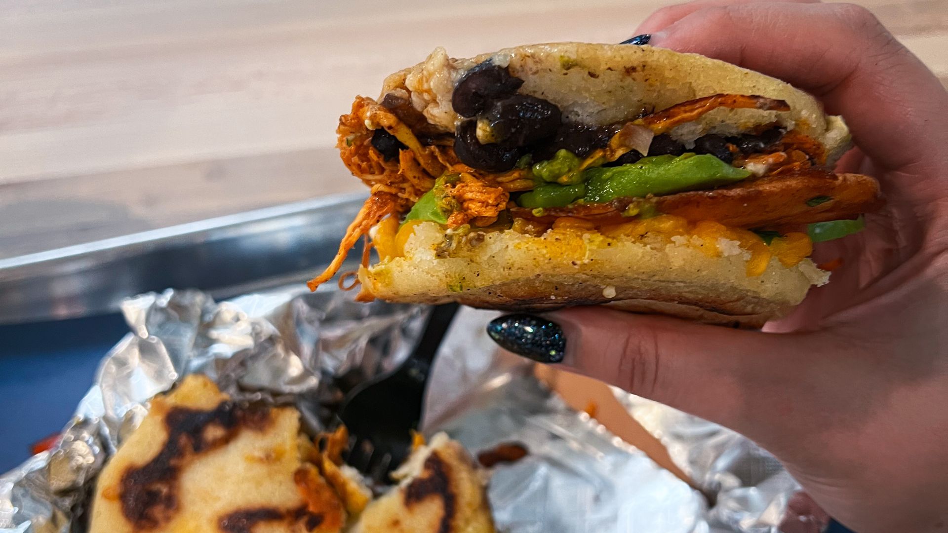 A hand holding up an arepa filled with goodies.