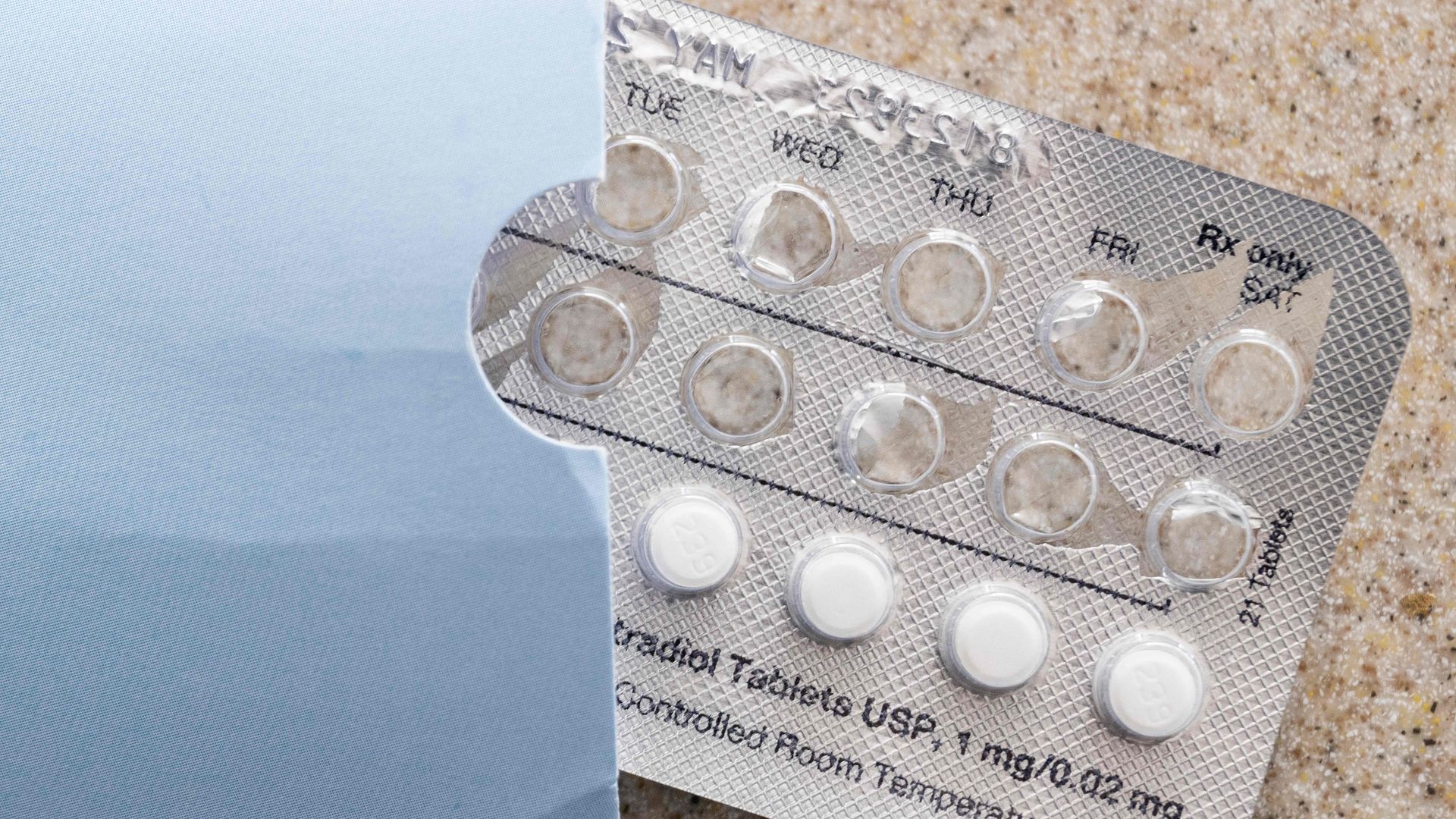 A pack of birth control pills sits on a counter, with four white pills visible.