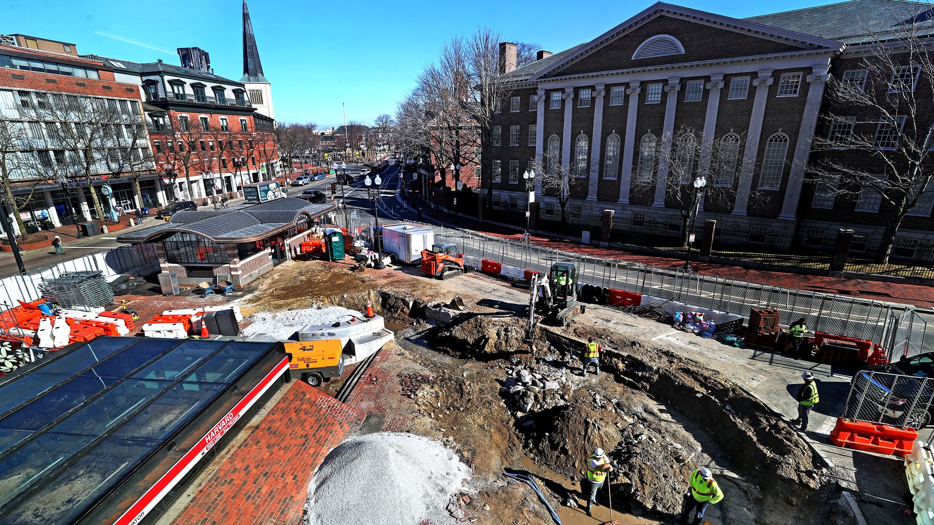 Overhead view of a big contruction pit with dirt, machinery, workers against the backdrop of brick buildings at Harvard.