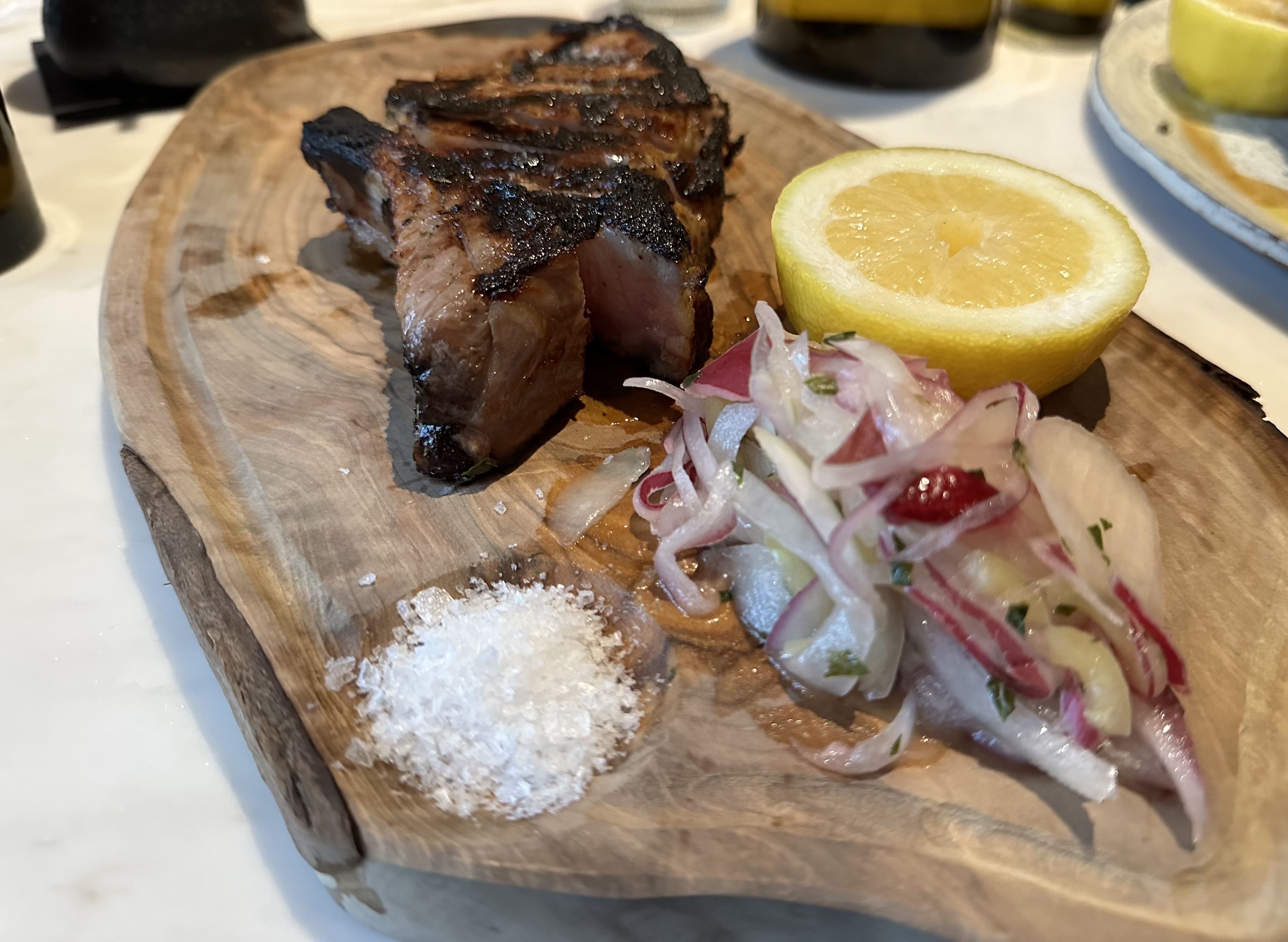 The pork chops are served with a side of salt, onions and lemon on a  wooden board.