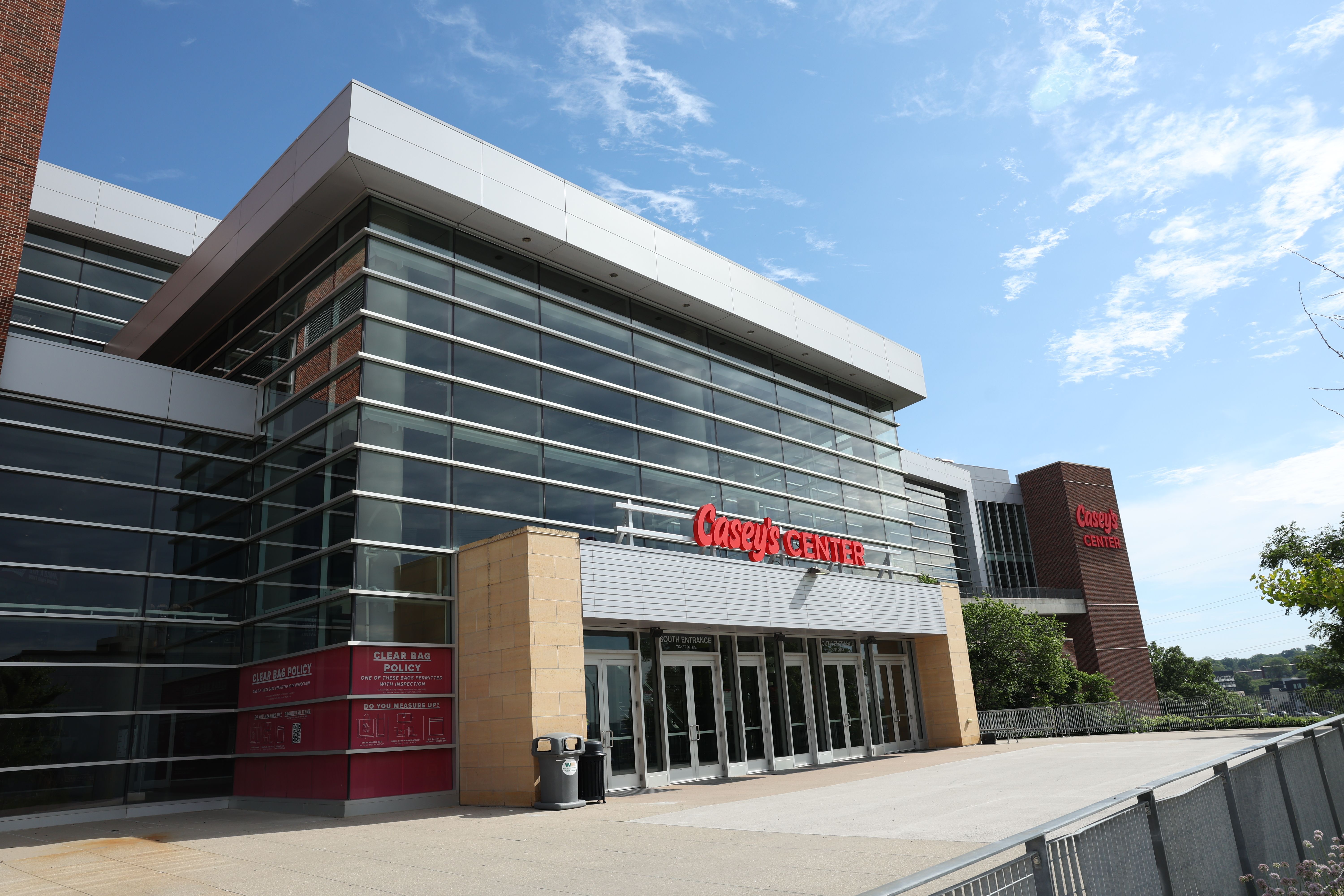 Modern glass-and-brick mall beneath a clear blue sky. A bright red sign reads "Casey's Center" above the entrance, with large glass windows and metal framing.