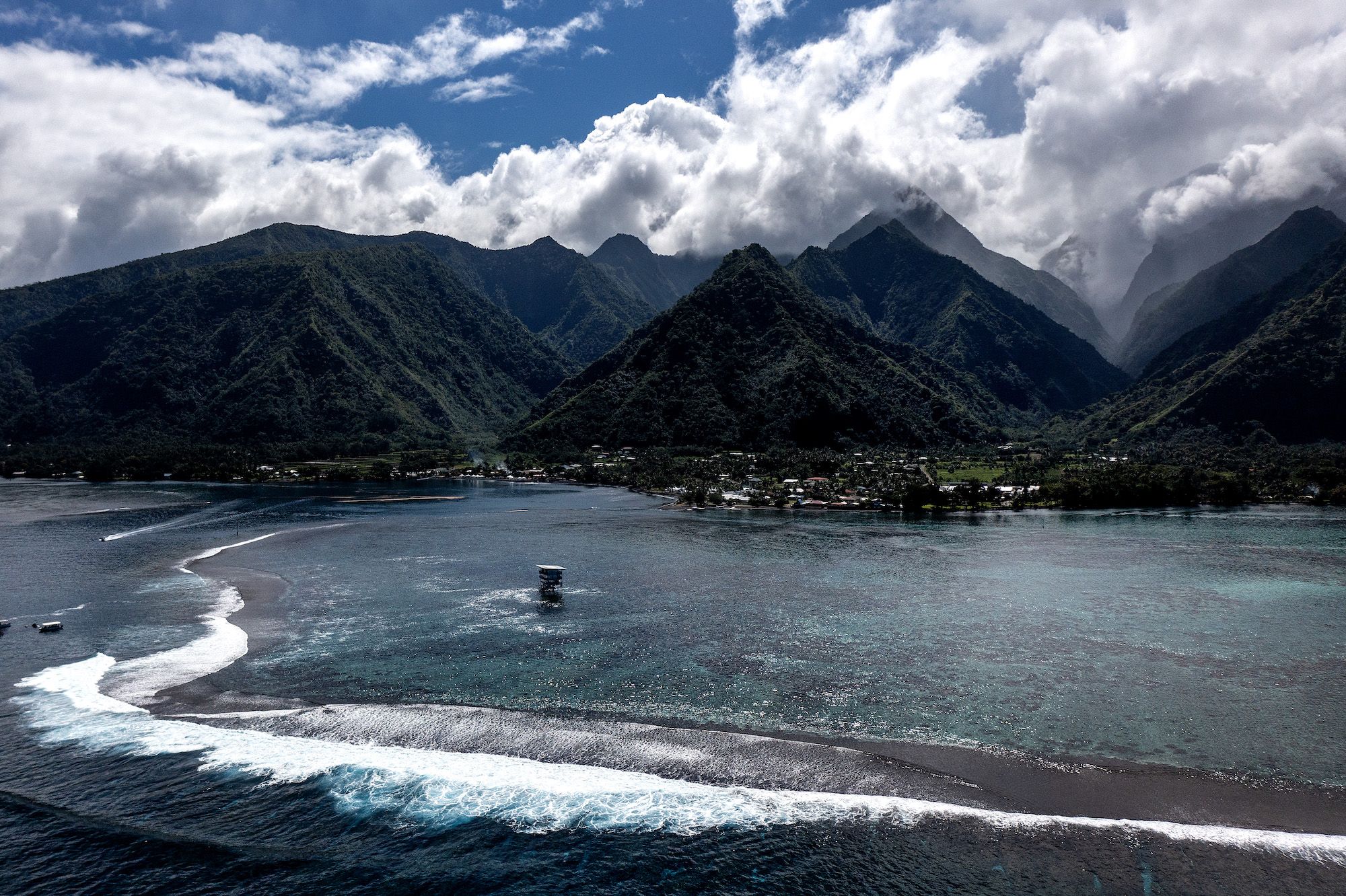 An aerial view of the coast of Teahupo'o showing the reef, waves and mountains.