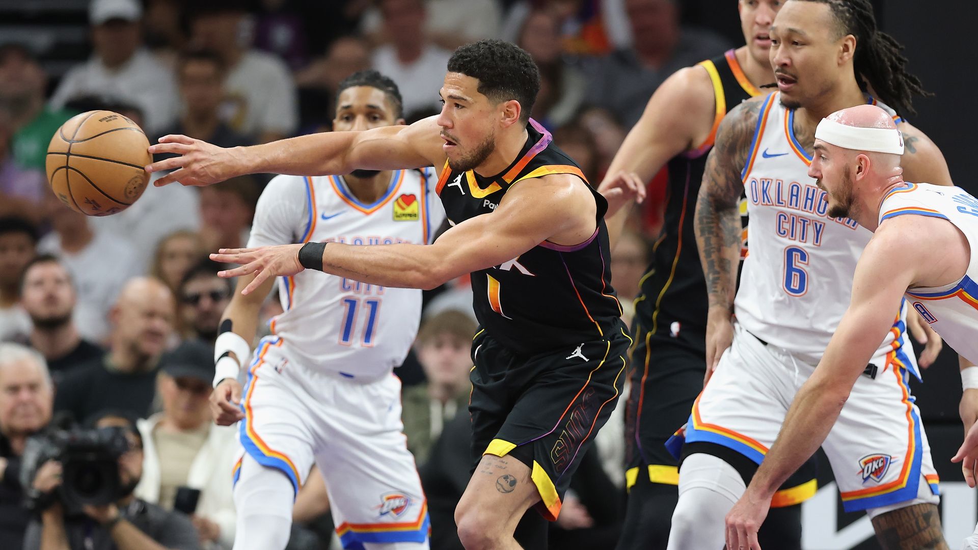 Devin Booker passes while surrounded by defenders from the Oklahoma City Thunder.