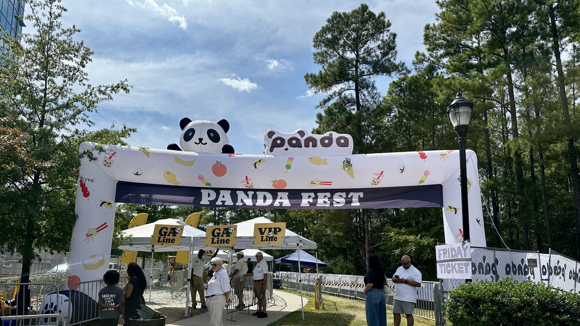 Outdoor entrance to Panda Fest with white inflatable arch decorated with food icons and a large panda figure on top, ticket booths labeled "GA Line" and "VIP Line," and people waiting.