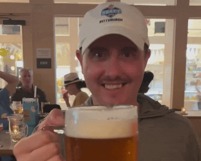 A man in a white cap holding a beer and clinking glass with the viewer.