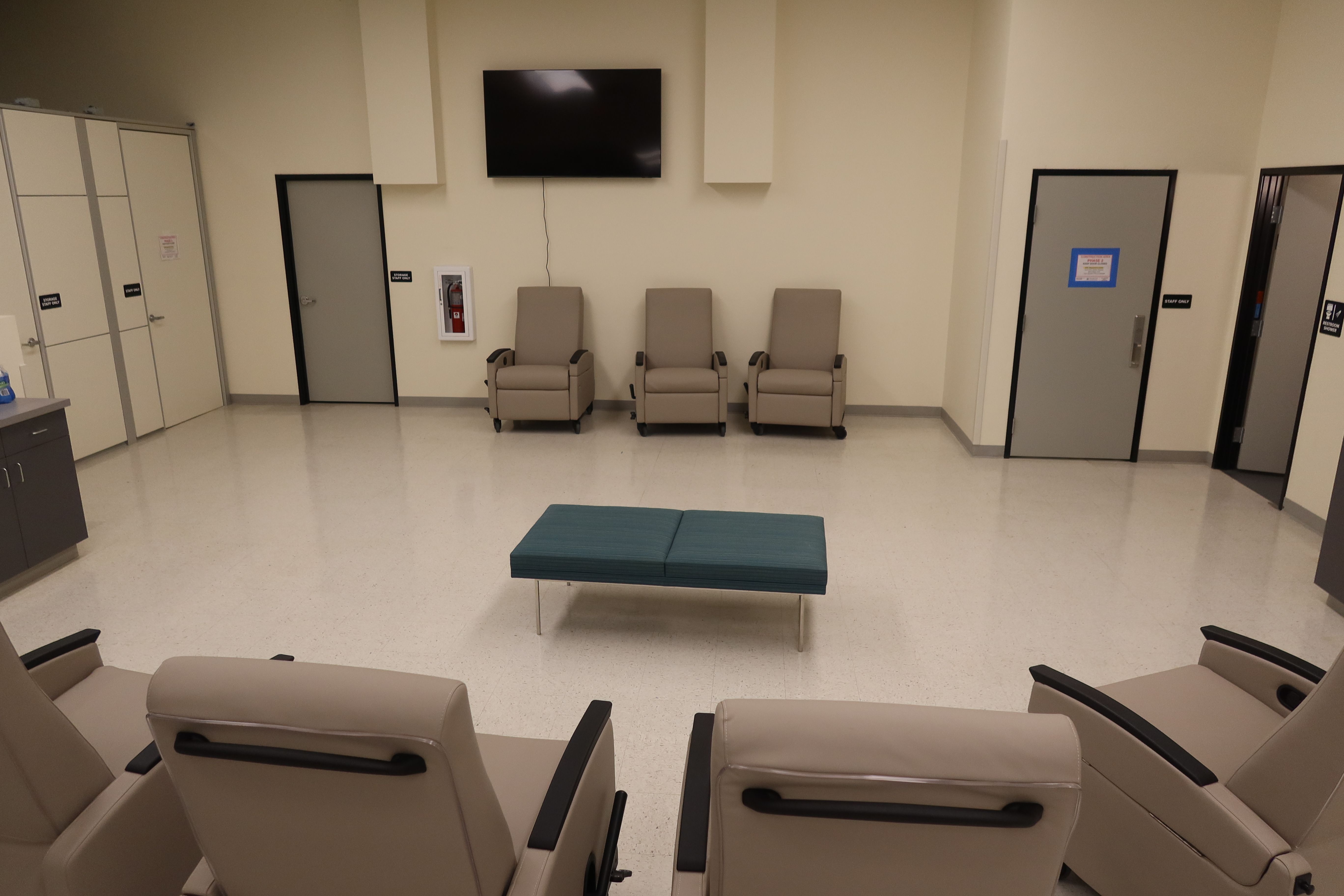 Several reclining chairs sit in a large room with a television on the wall.