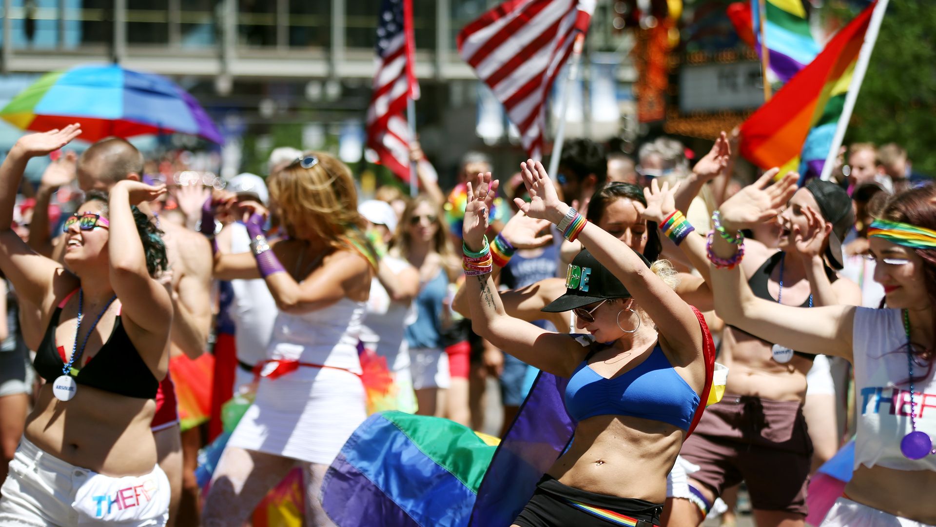 A group of people dancing in the street waving pride flags.