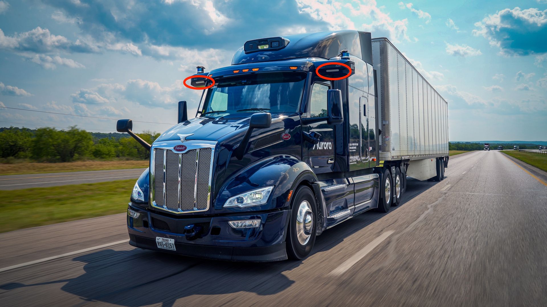 Image of an autonomous Aurora semi-truck, with red circles highlighting the lights  on the cab that could be illuminated to warn other drivers if it is stopped on the shoulder of the highway. 