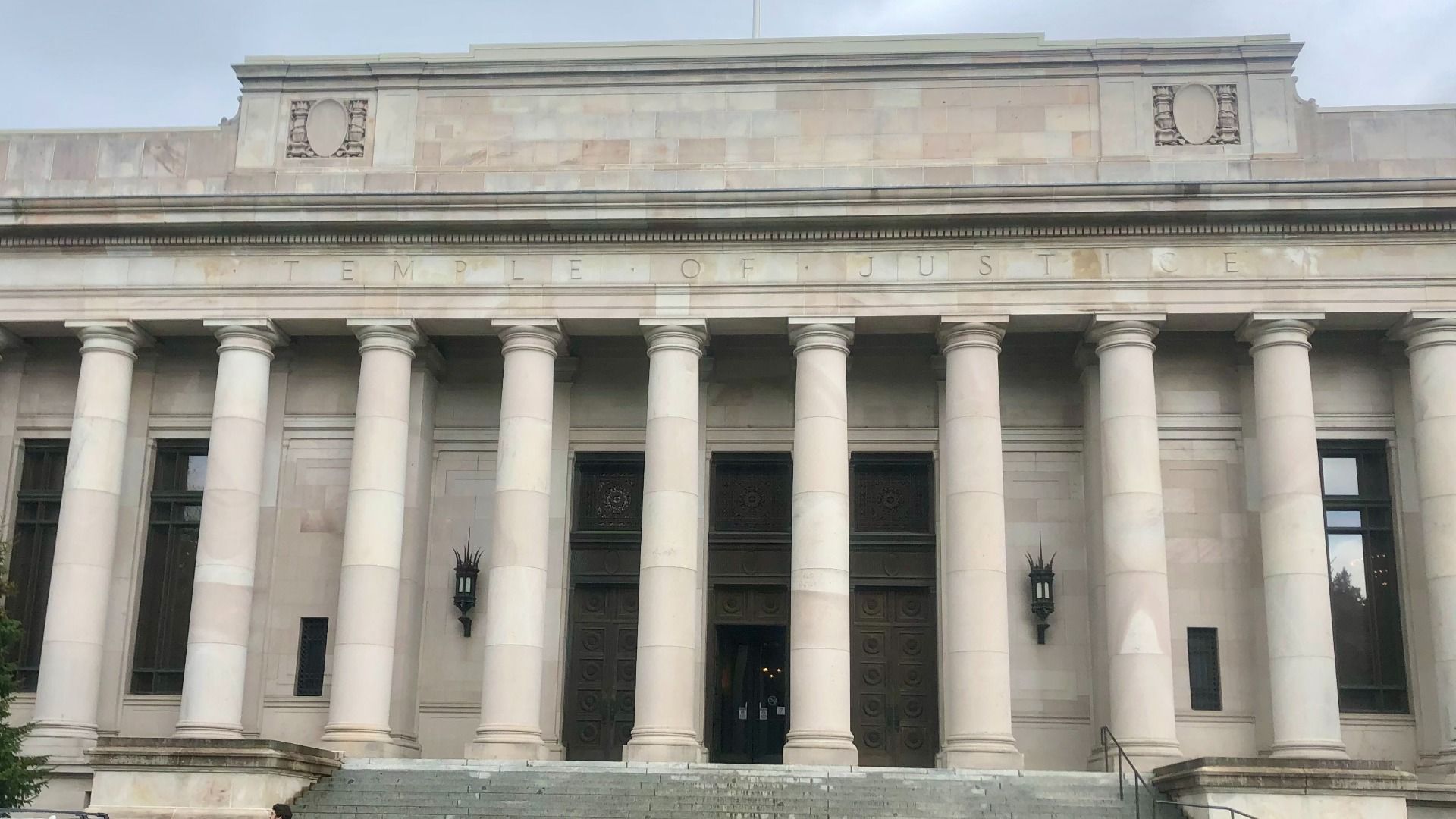 Front view of a neoclassical courthouse with a row of tall white columns, wide stone steps, and the inscription "TEMPLE OF JUSTICE" along the frieze.