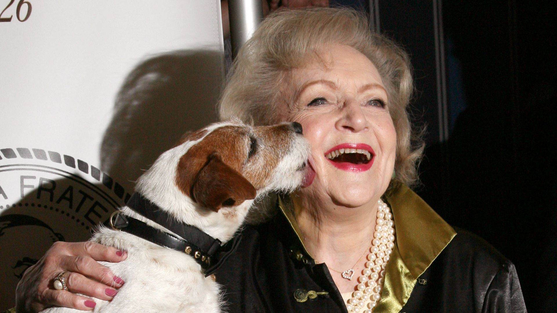 A dog licks Betty White's face as she smiles
