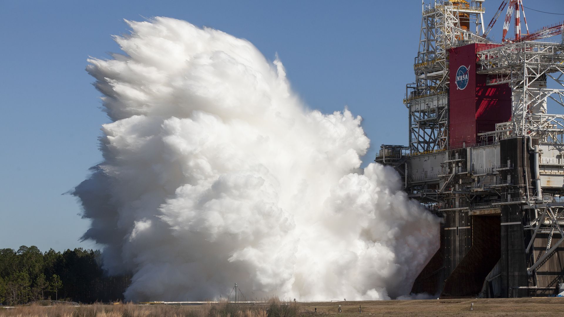 A plume of white smoke coming from a rocket strapped to a pad at NASA