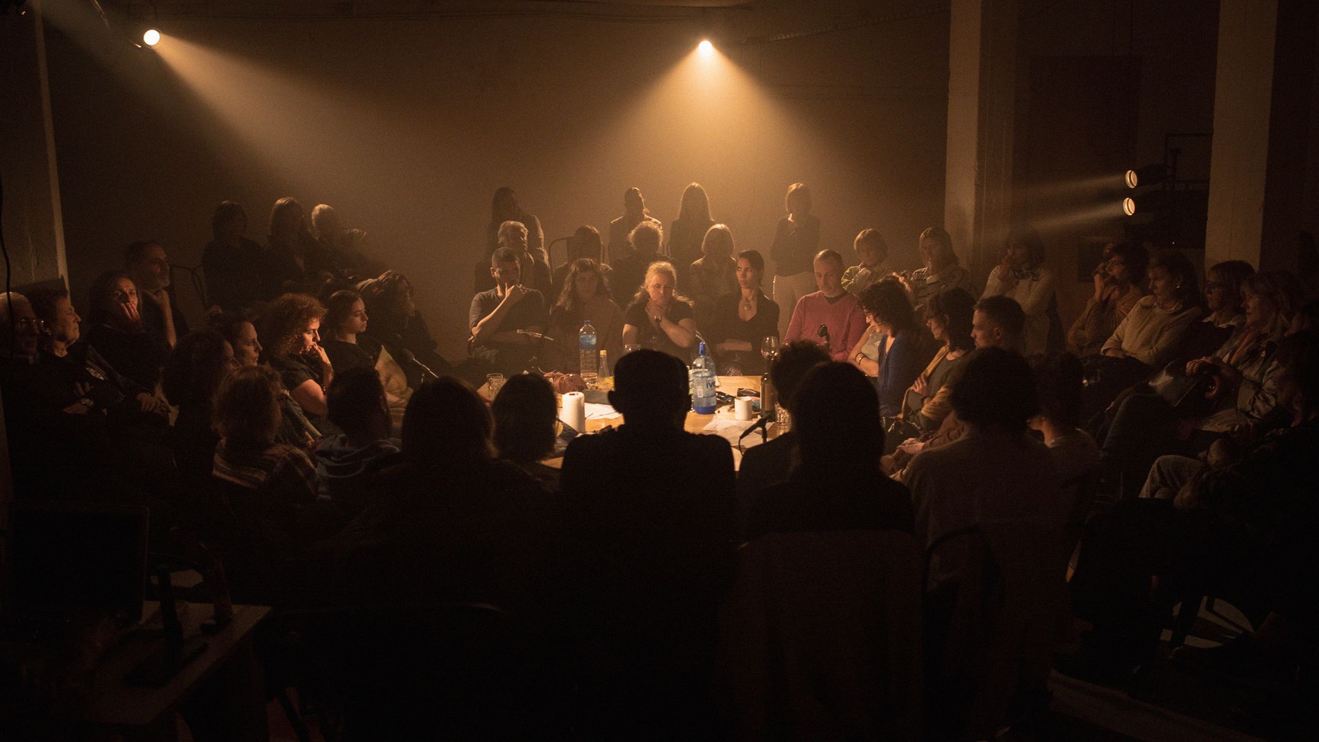 The cast of the play "gaviota" sit at a table, surrounded by audience members 