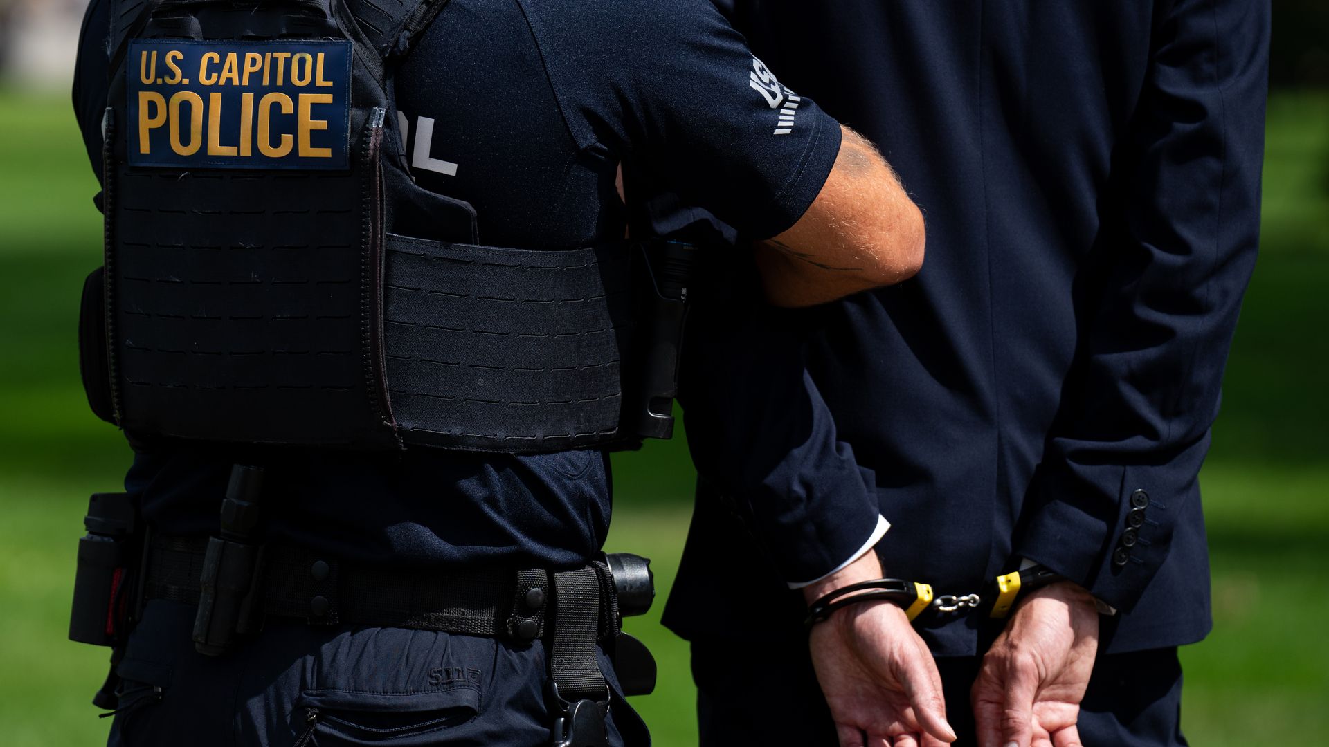 A US Capitol Police officer holding a man's arm, who is wearing a blue suit, in handcuffs. No faces are featured in the photo. 