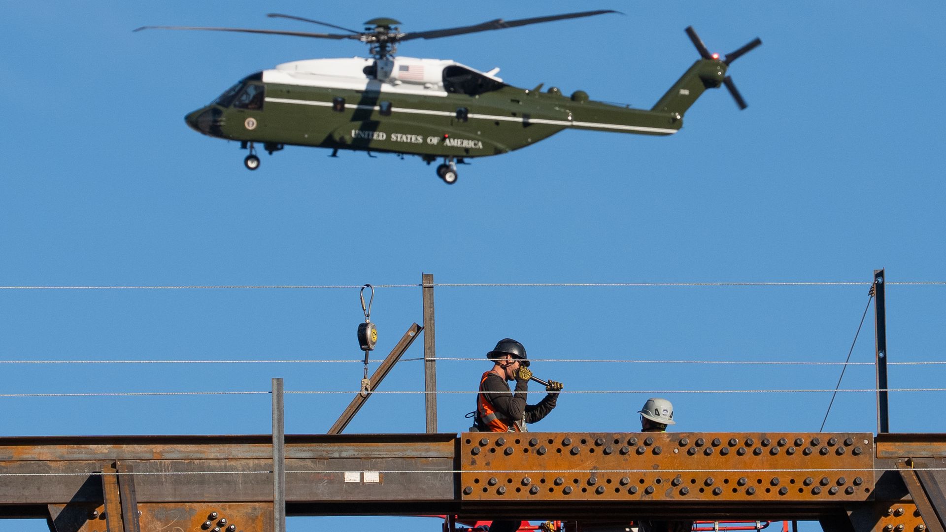 Marine One in the background in a bright blue sky, with the White House ballroom under construction in the foreground