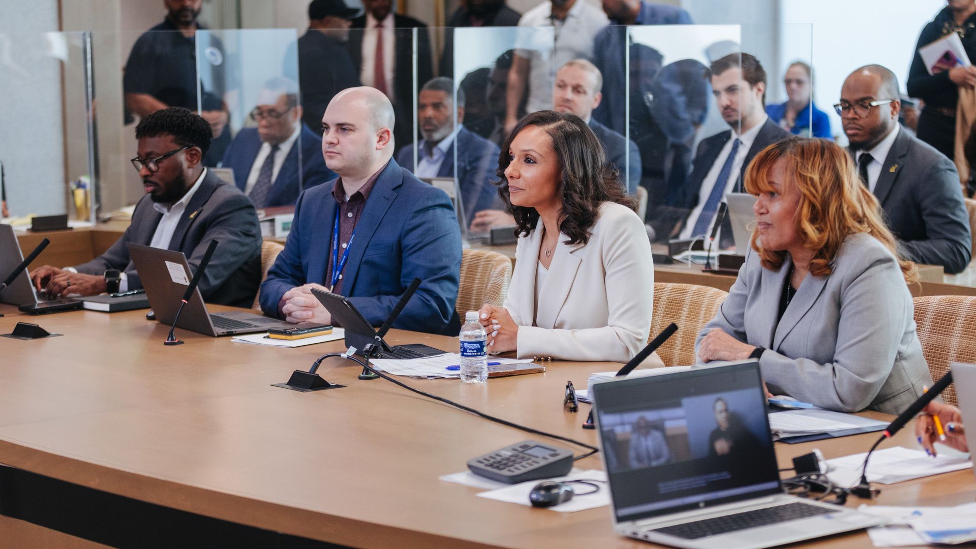 City officials including the mayor sit beside a conference table with laptops and microphones.