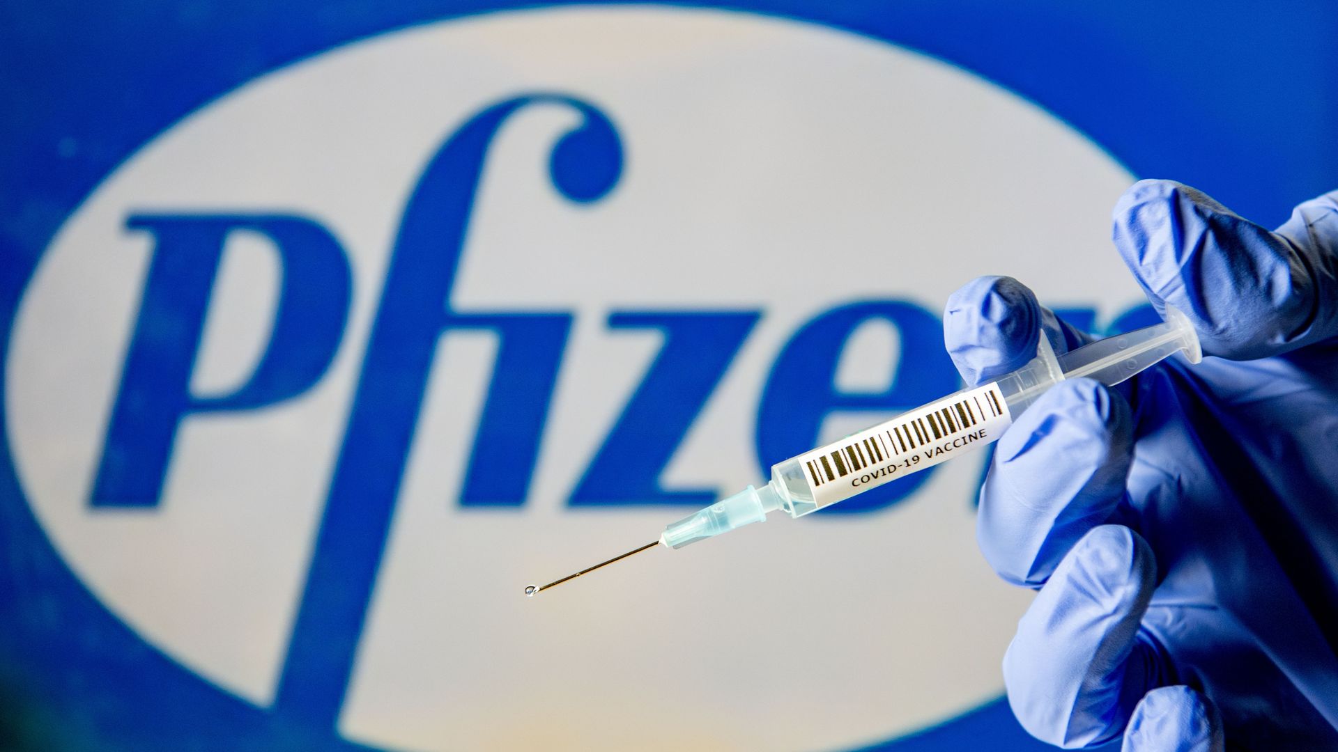 Picture of a hand holding a syringe in front of a Pfizer sign