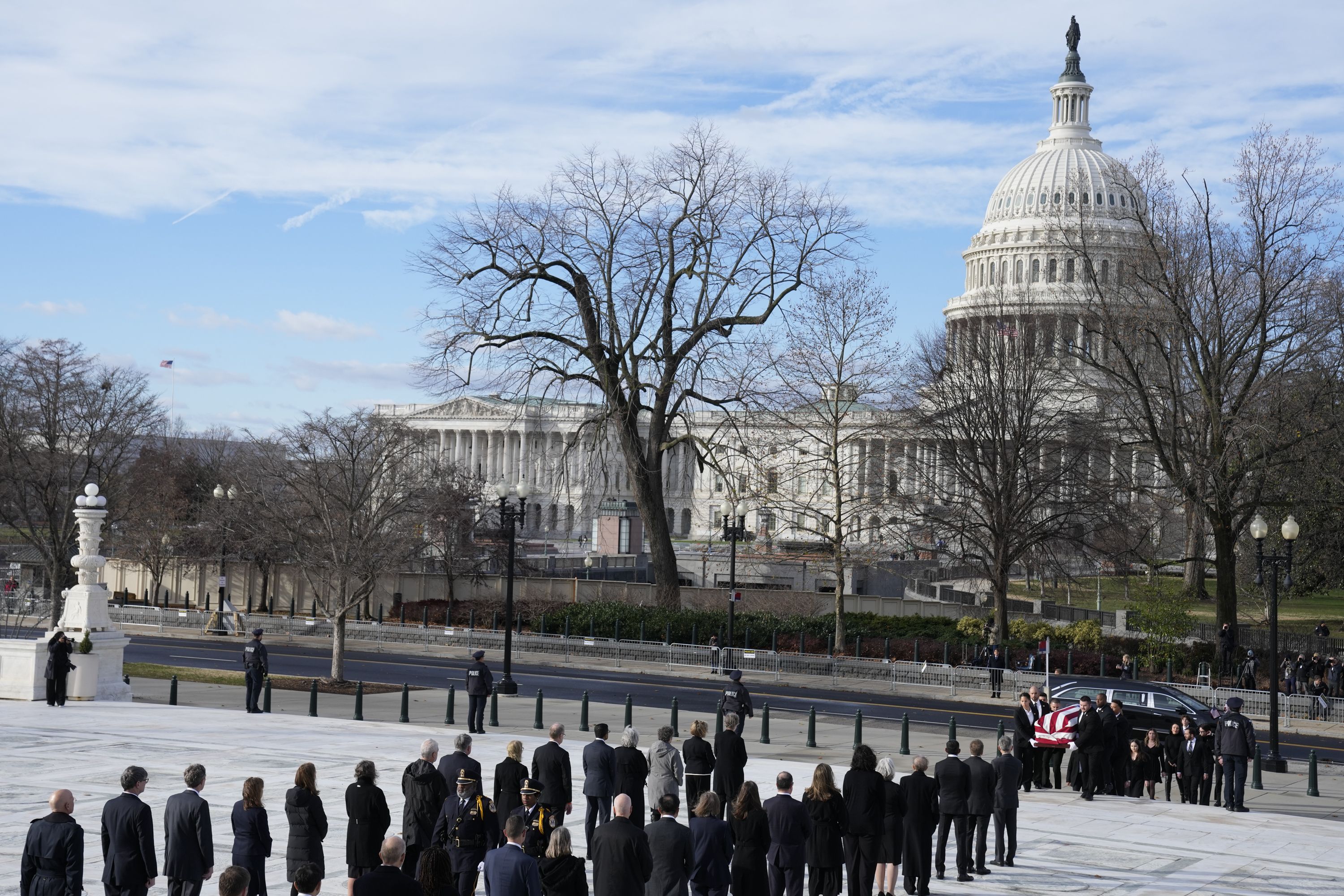 Dozens of people in a line as O'Connor's casket is held by six or so people. it is covered with an American flag.