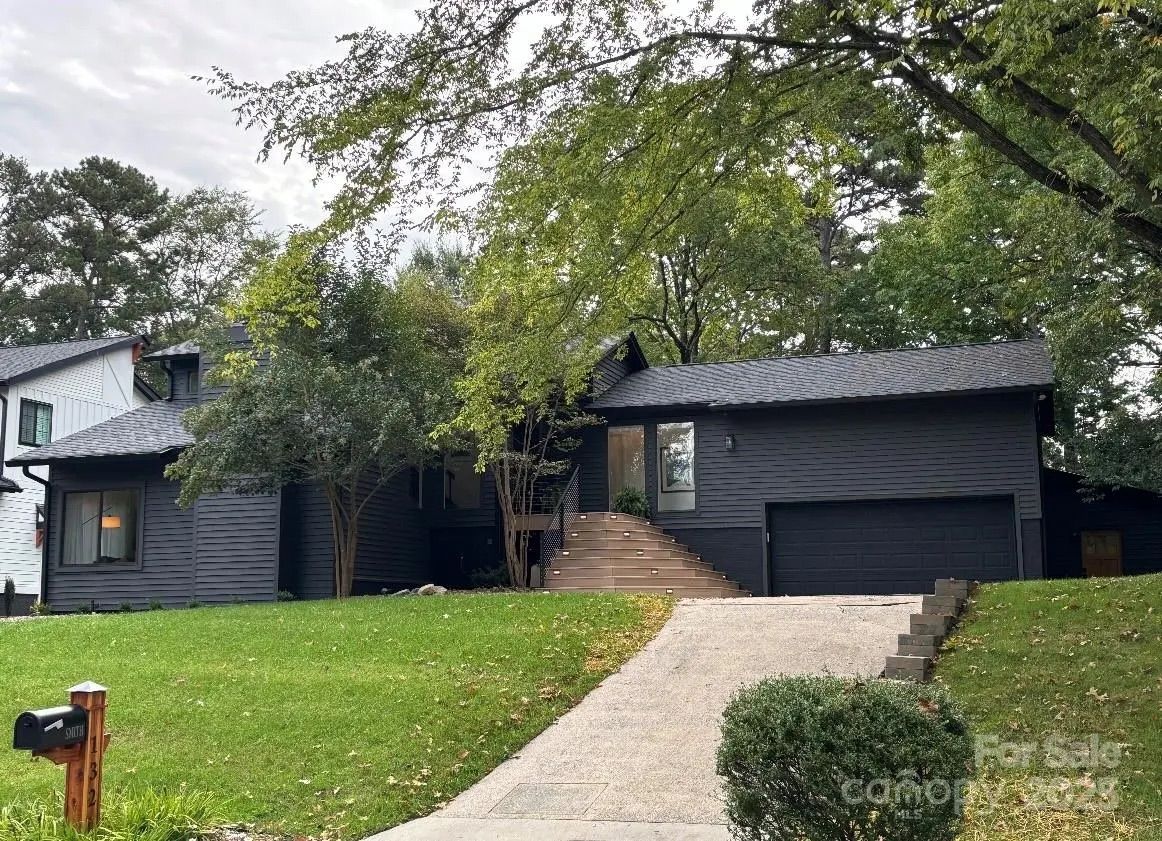 Modern dark gray house with front stairs, large driveway, green lawn, trees, and a black mailbox with house number 305. Adjacent white house partially visible on the left.