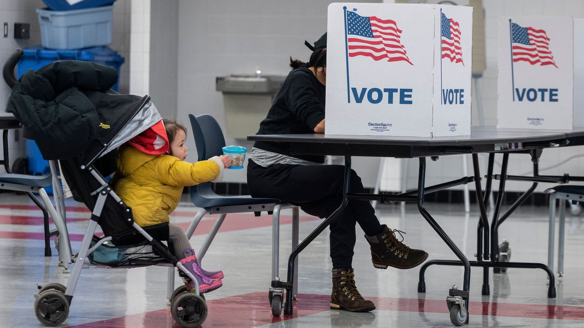 A toddler is seen placing their snack on a table as an adult casts a ballot in the Virginia election.