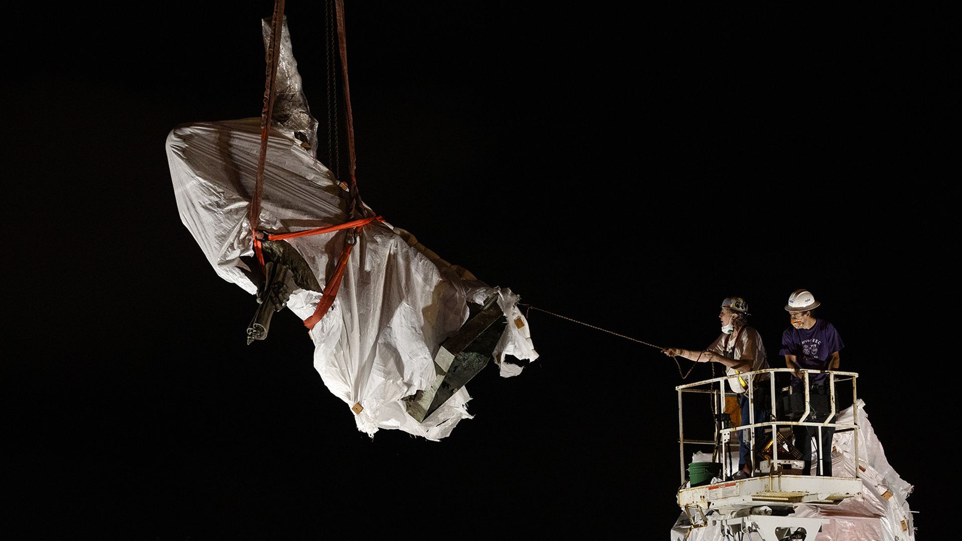 Crews hoist a cloth-covered Columbus statue from the ground. 