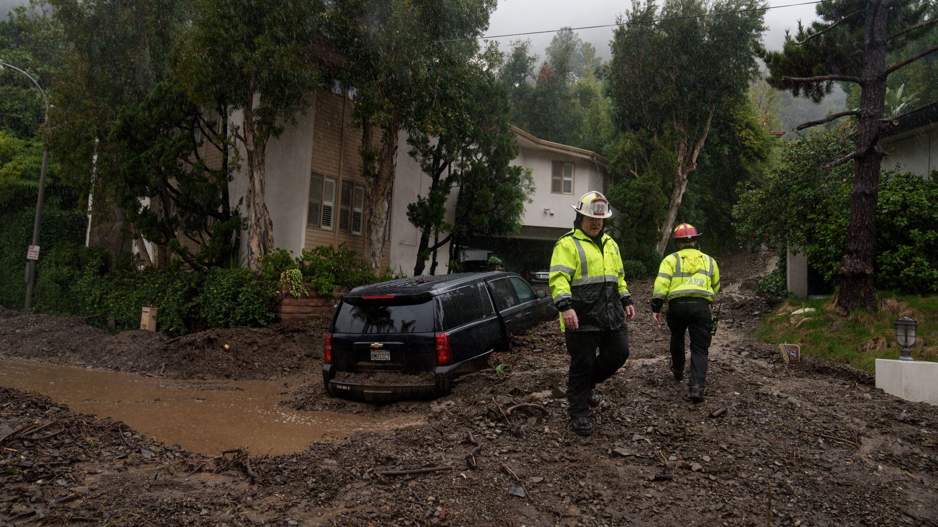 Picture of an SUV stuck in mud and water with two rescue workers amid a California rainstorm.