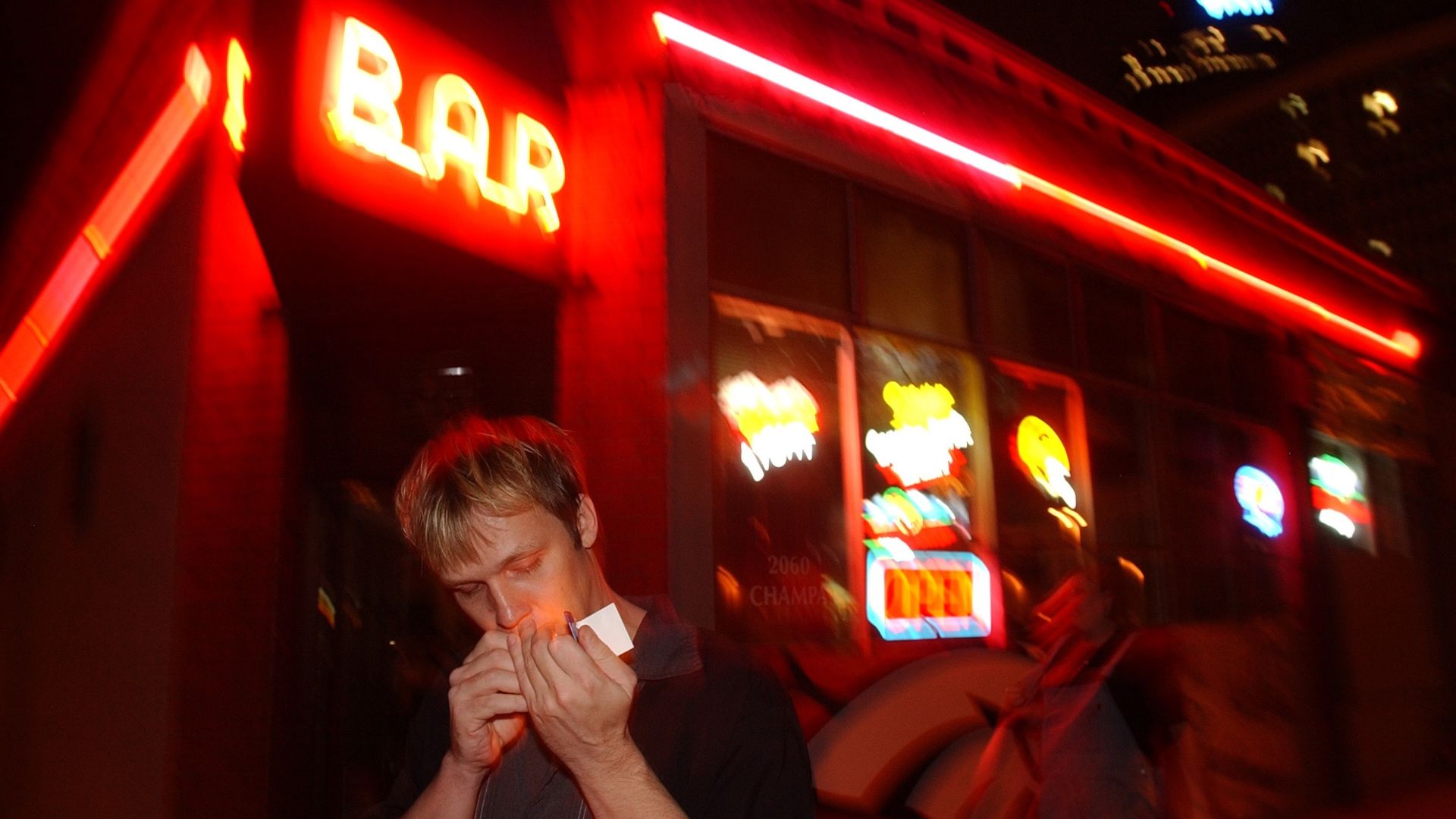 A man stands outside the bar known as Bar Bar in downtown Denver at night