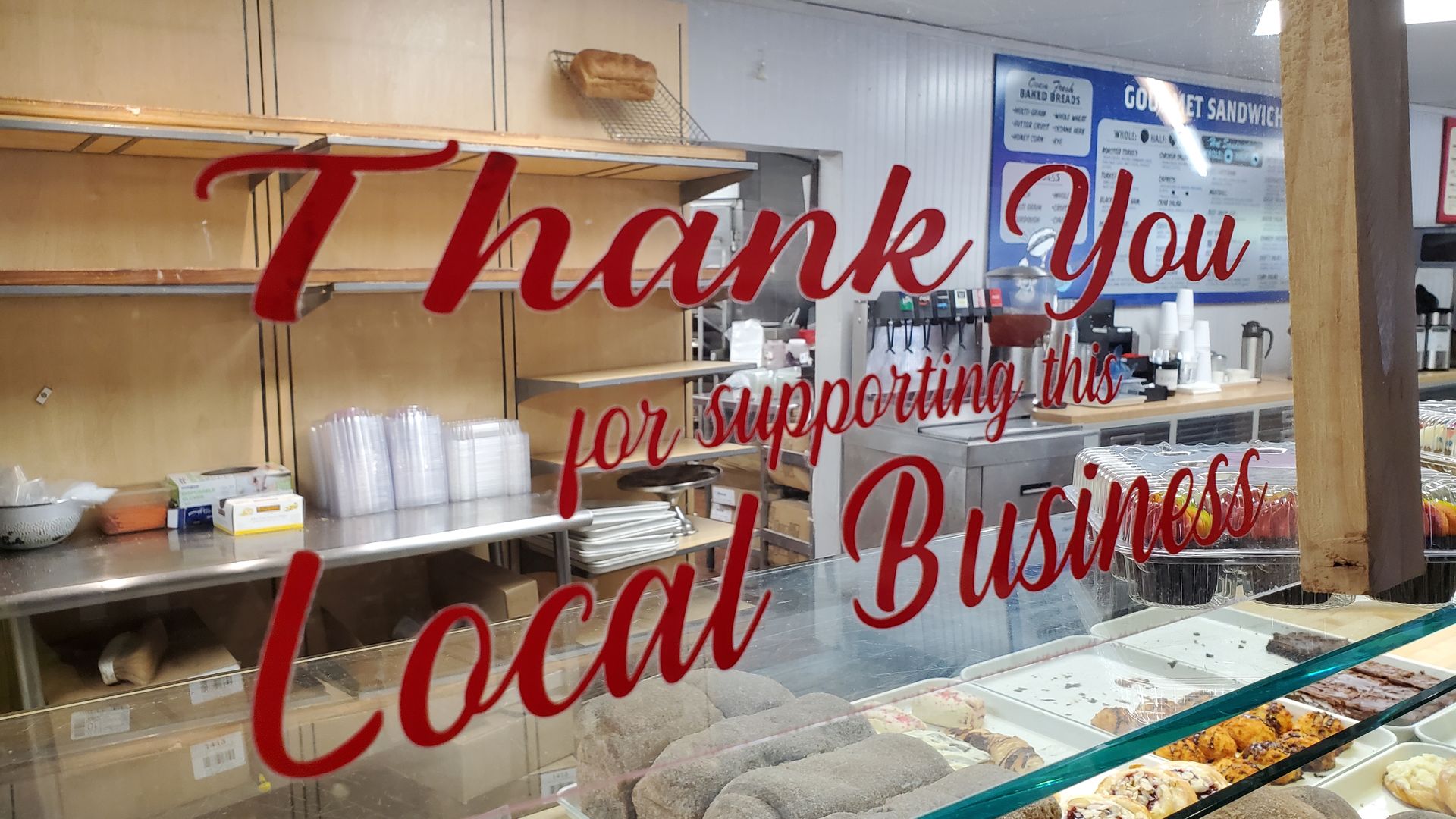 Red text thanking customers for supporting a local business is emblazoned on a glass window that sees into a small business.