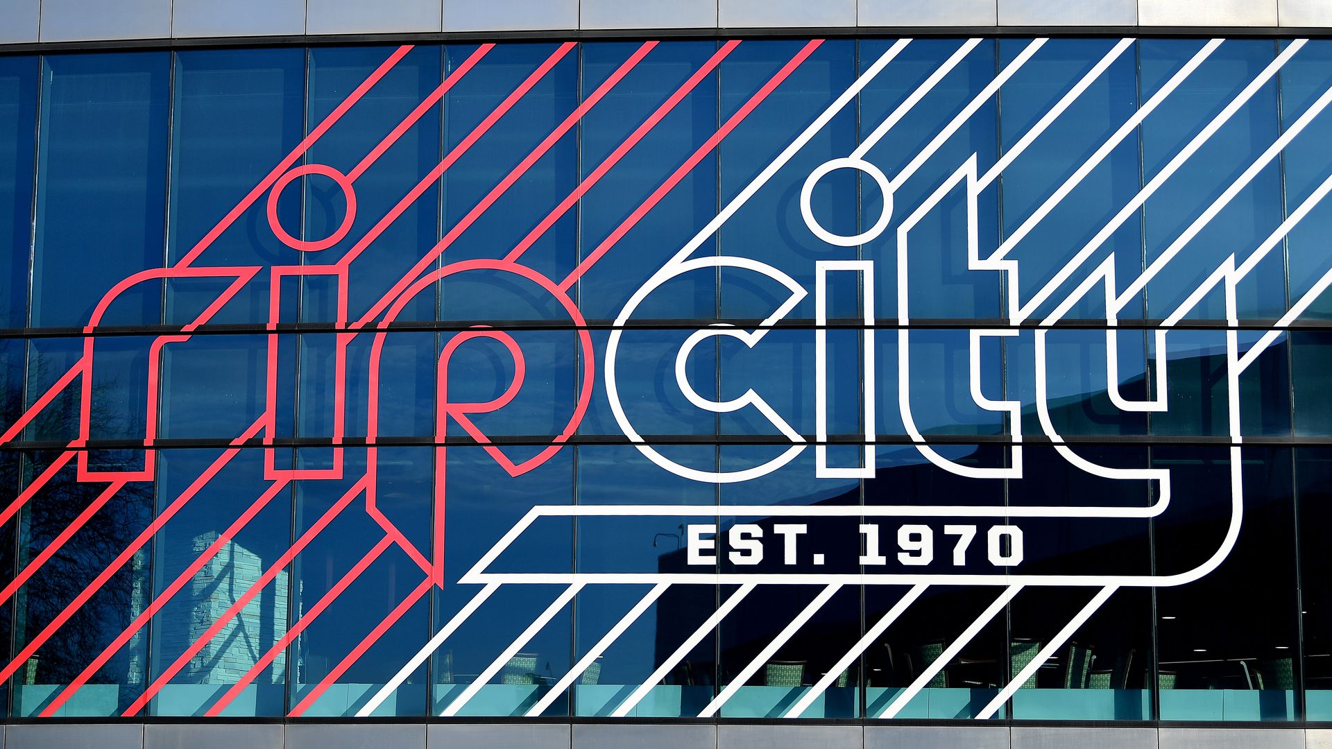 Glass building facade with a large sign reading "rip city" in red and white lines, and "EST. 1970" in white block letters beneath.