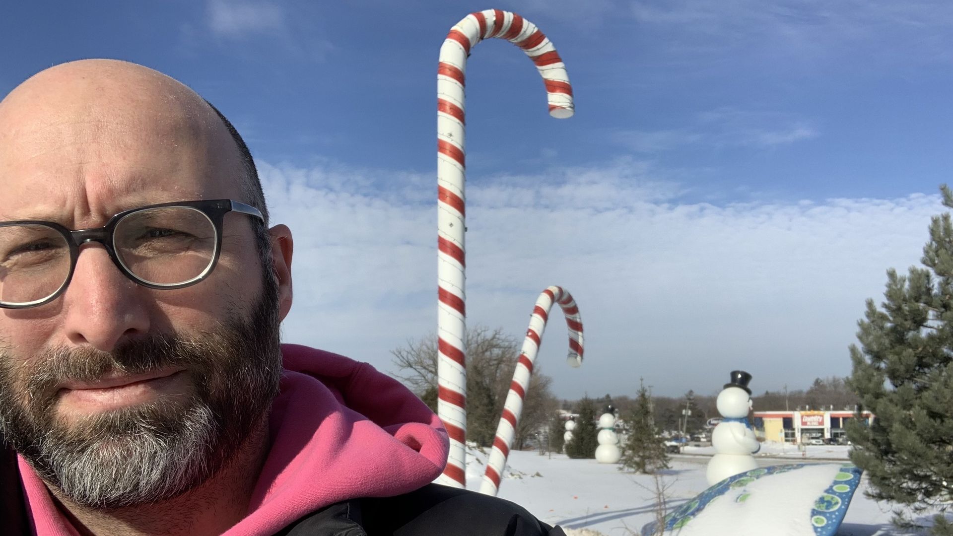 Photo of a man standing in front of a giant candy cane. 