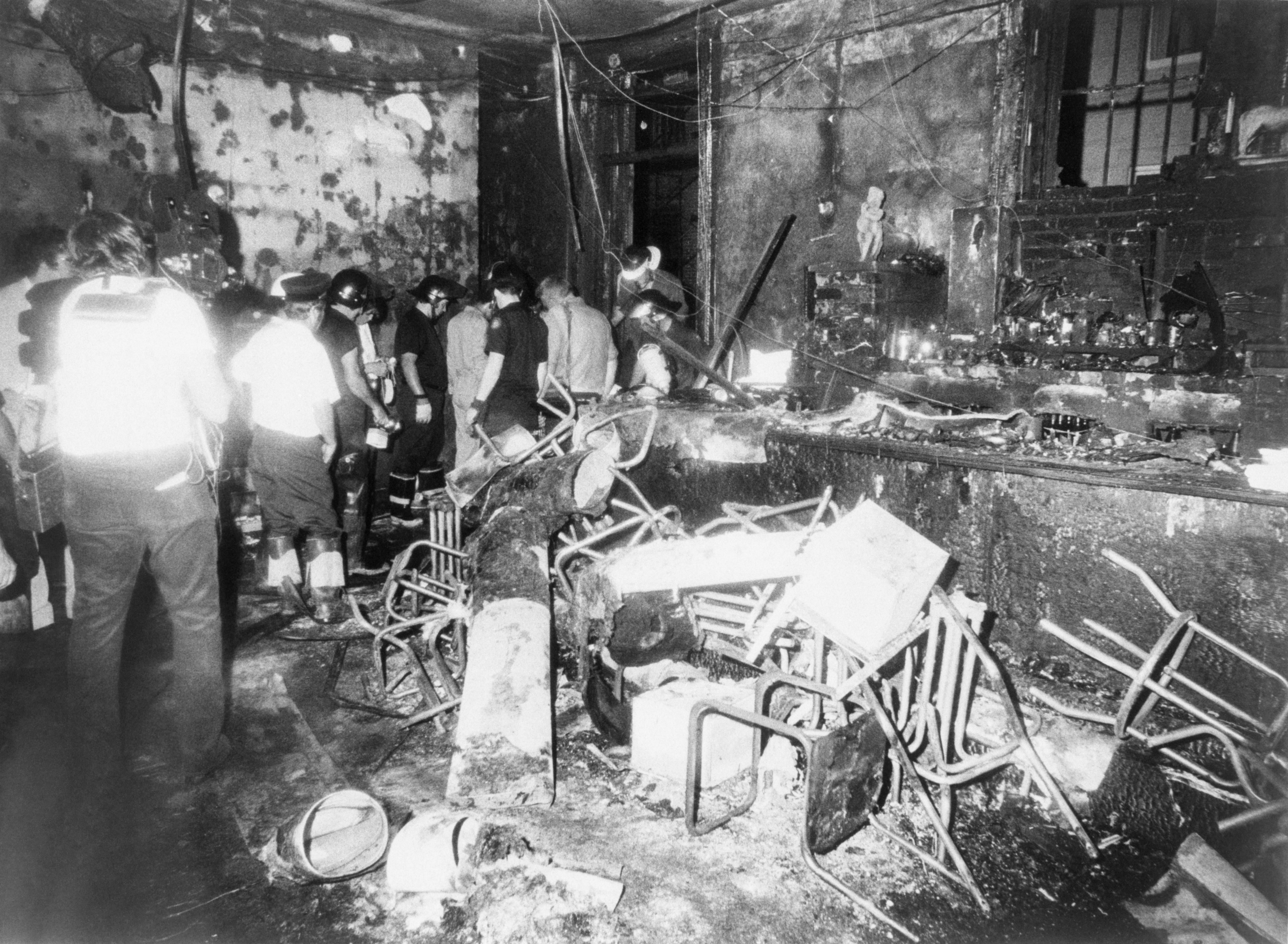Image shows men walking through a burned bar with overturned chairs.