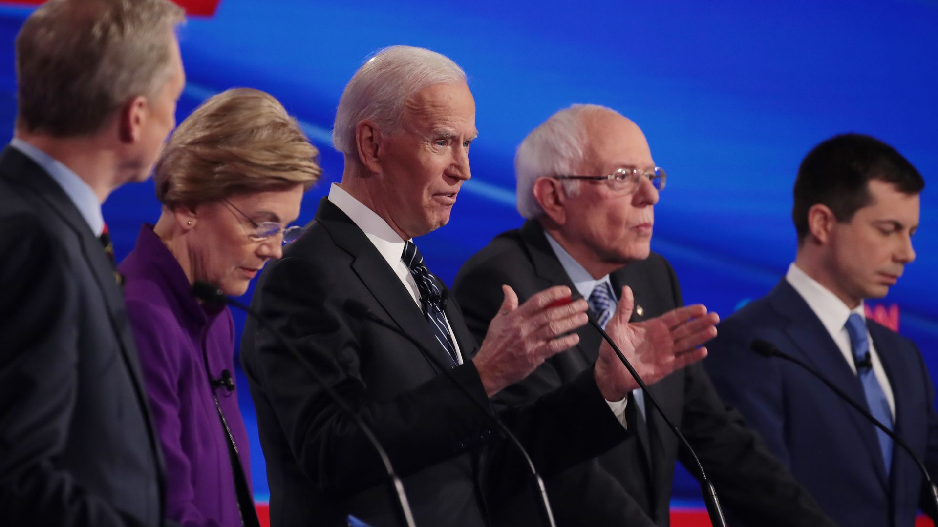 In this image, Tom Steyer, Elizabeth Warren, Joe Biden, Bernie Sanders, and Pete Buttigieg stand in a line.
