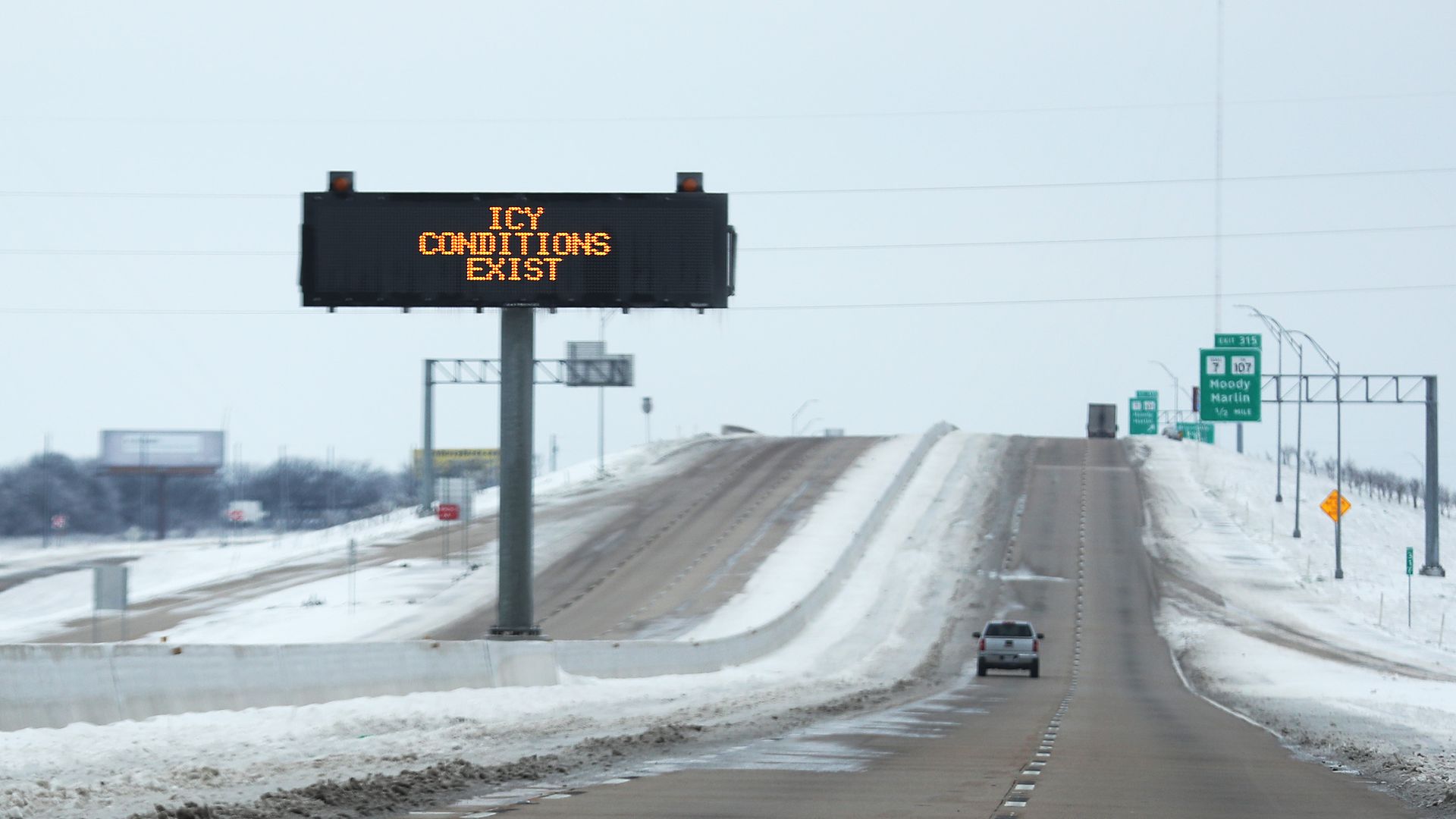 Picture of a road with snow covering each side, and a sign stating "Icy Conditions Exist."
