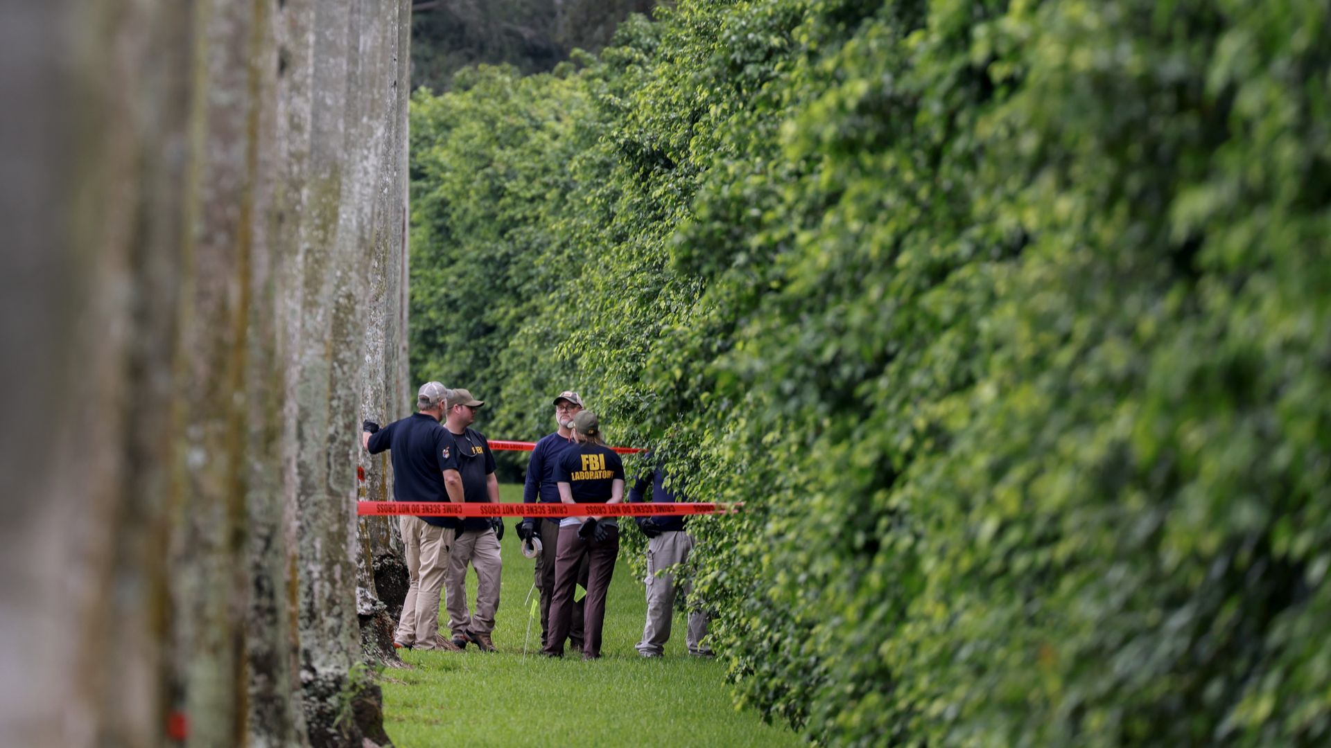 Federal investigators stand near trees behind crime scene tape