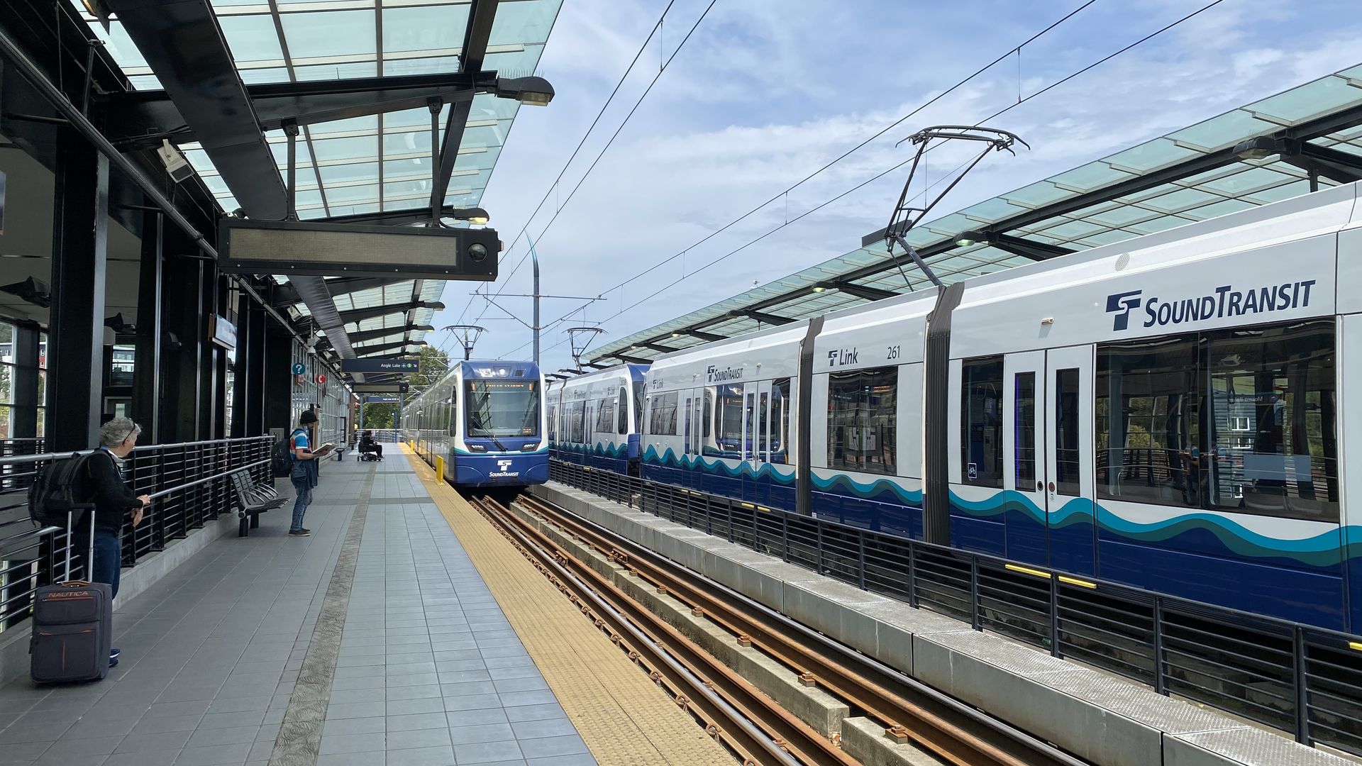 A Sound transit train goes by in one direction while another comes in the other direction at a light rail platform. 